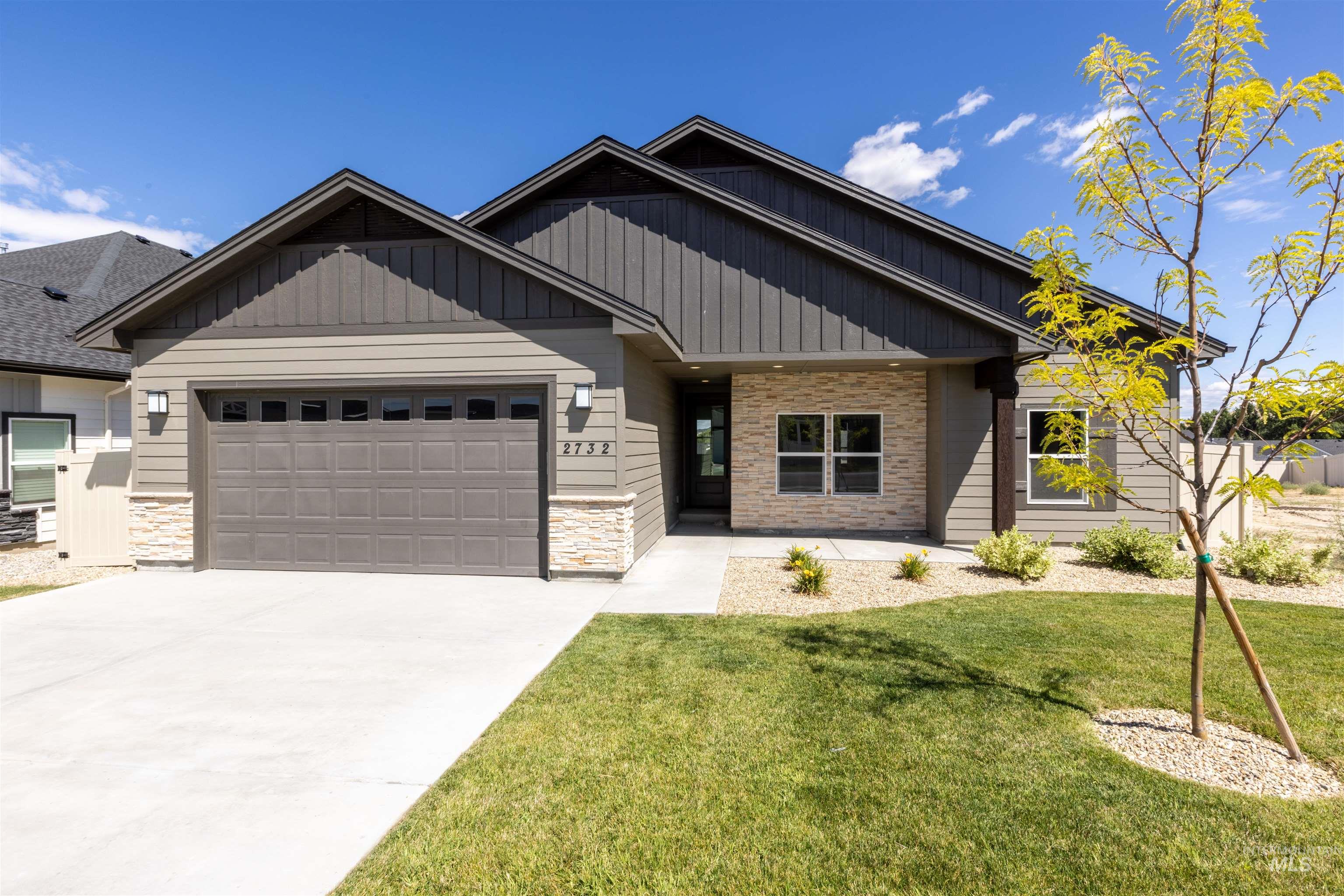Craftsman-style home with an attached garage, stone siding, concrete driveway, and a front lawn