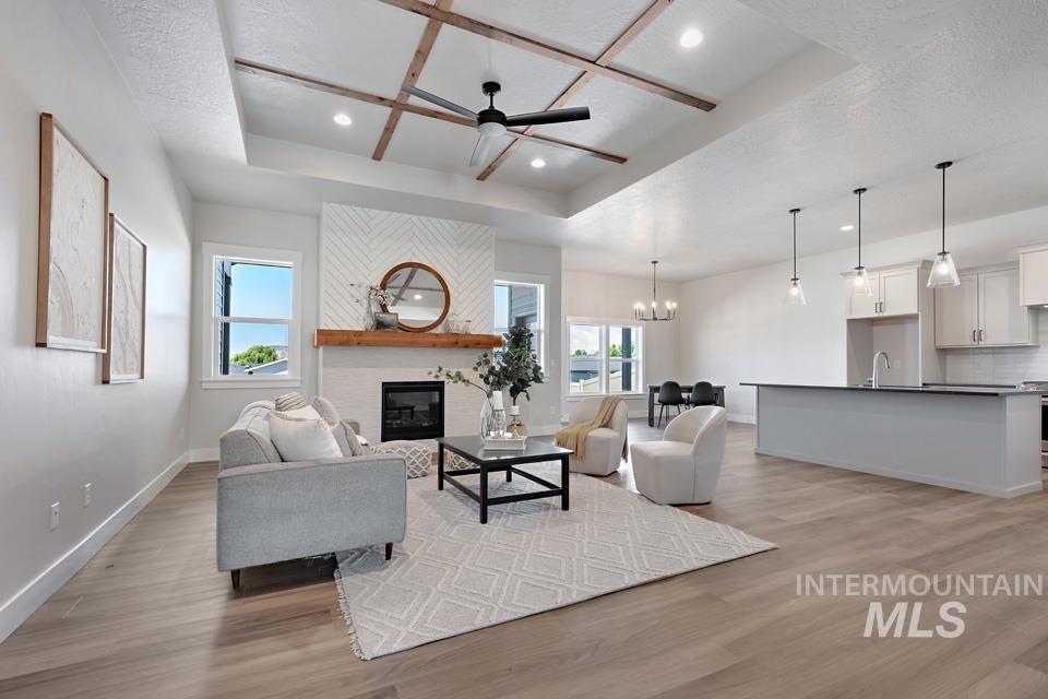 Living area with a raised ceiling, ceiling fan, light wood-style floors, a large fireplace, and recessed lighting