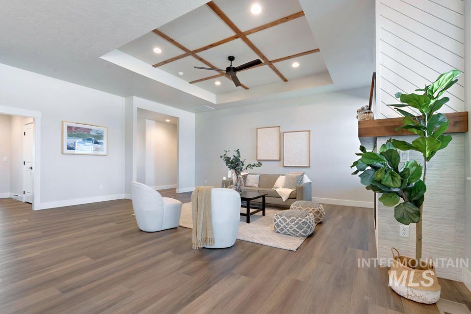 Living room with a tray ceiling, wood finished floors, ceiling fan, and recessed lighting