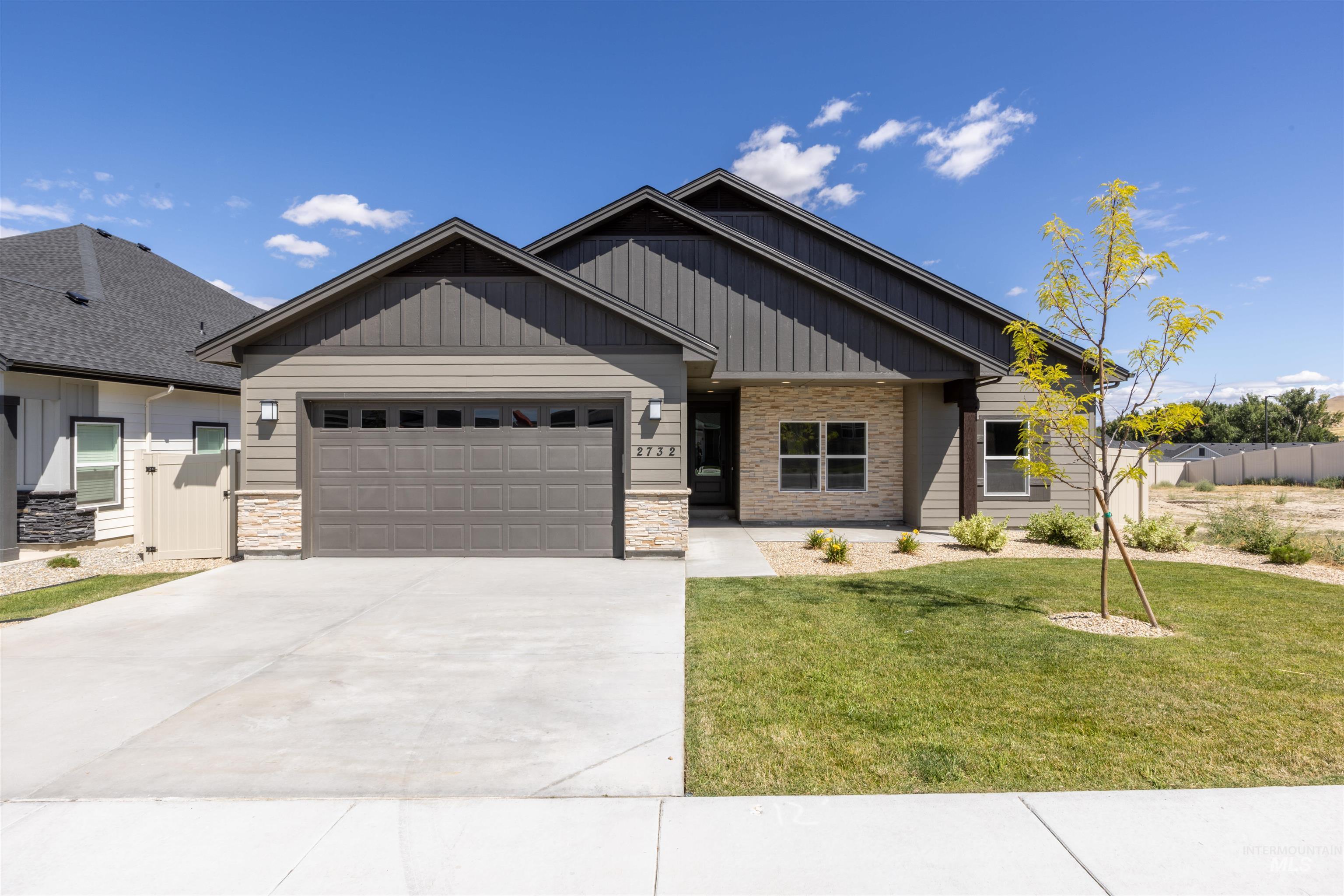 Craftsman-style house with stone siding, a garage, driveway, and board and batten siding