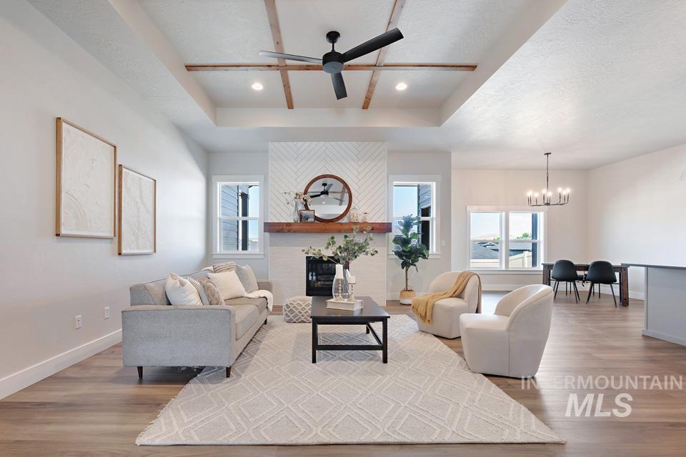 Living room with a raised ceiling, a ceiling fan, a fireplace, recessed lighting, and wood finished floors
