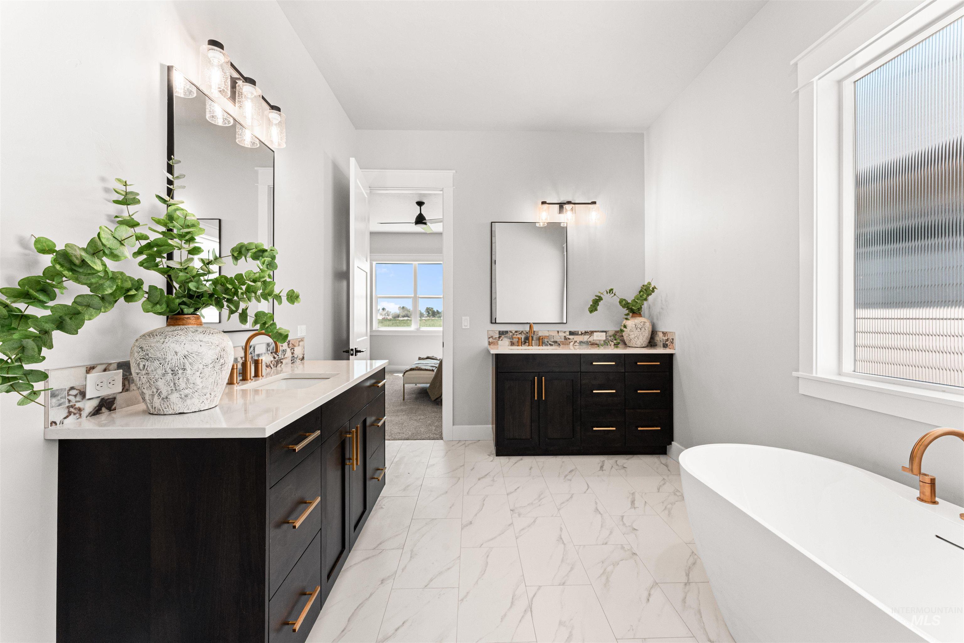 Full bath featuring two vanities, a freestanding bath, a ceiling fan, and marble look tiles