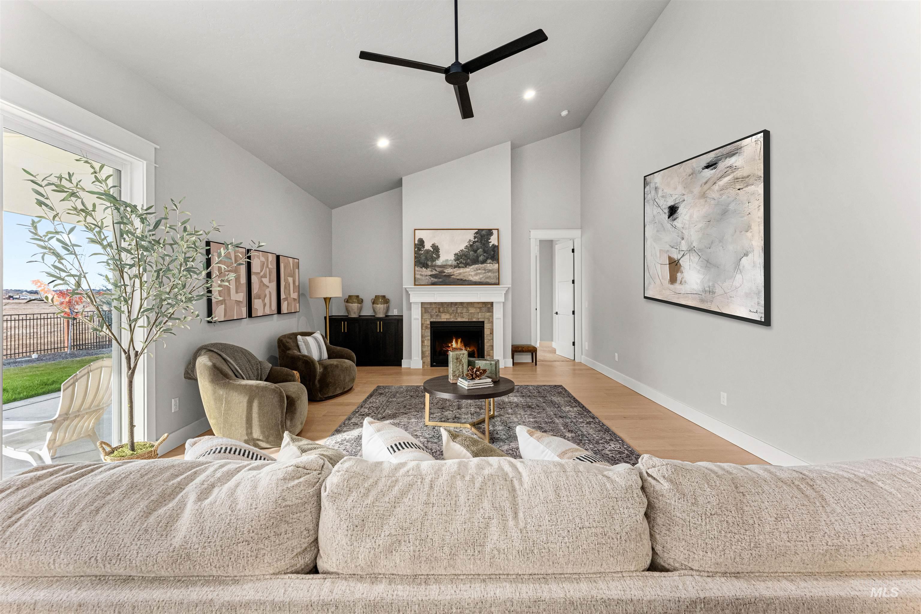 Living area with a lit fireplace, high vaulted ceiling, wood finished floors, recessed lighting, and a ceiling fan