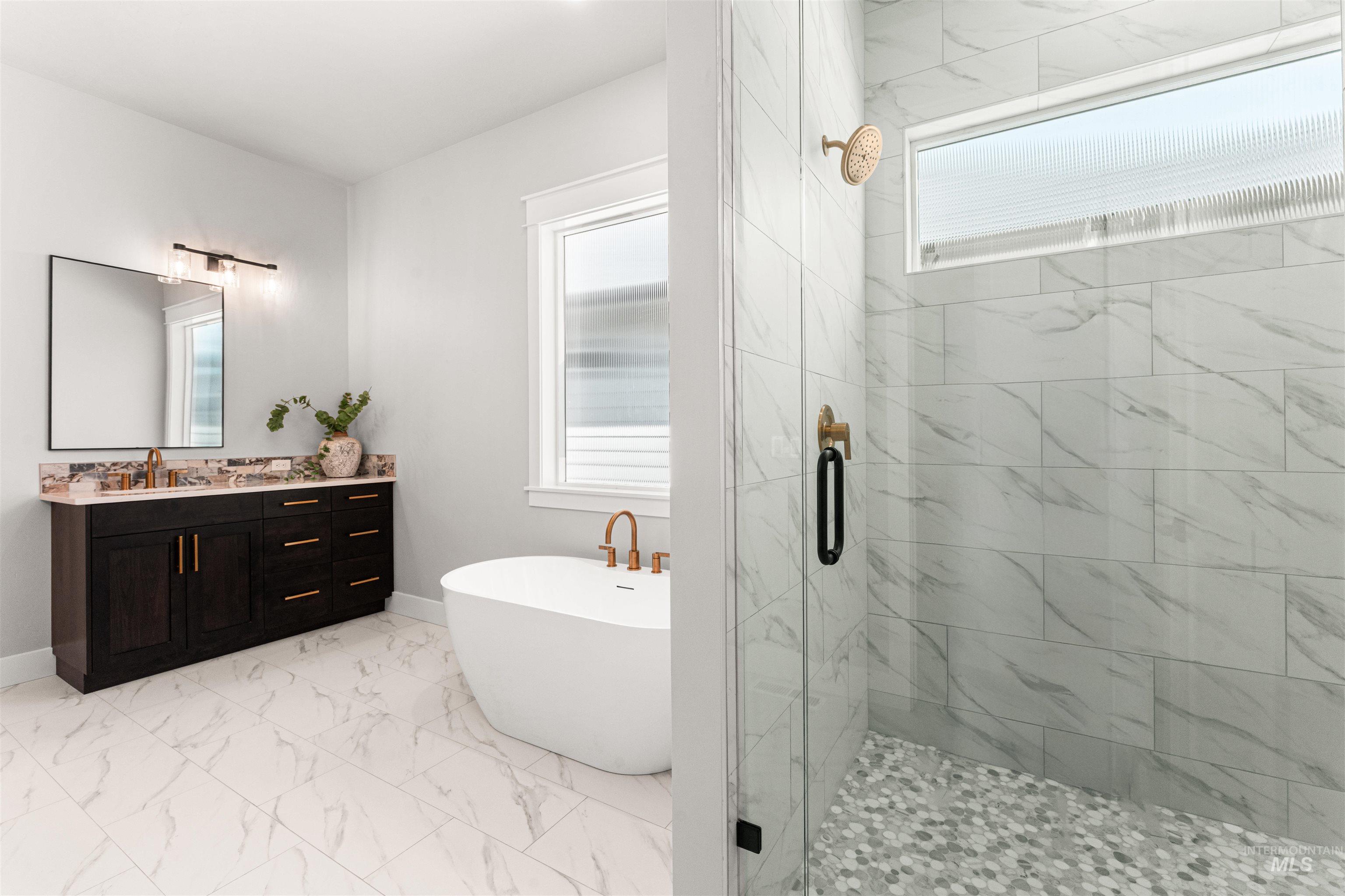 Bathroom featuring a stall shower, a freestanding tub, vanity, and marble look tiles
