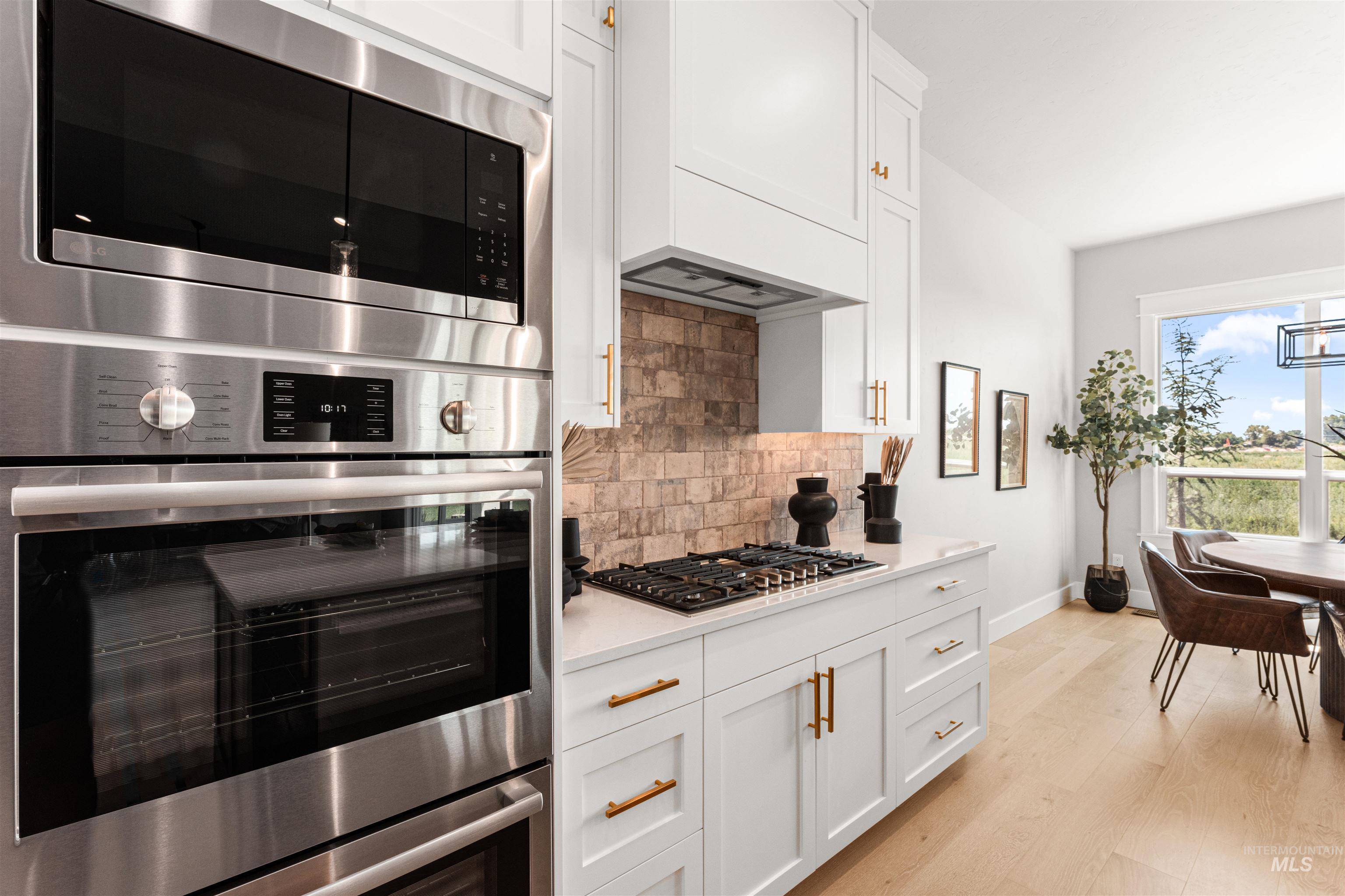 Kitchen with stainless steel appliances, decorative backsplash, white cabinetry, and light wood-style floors