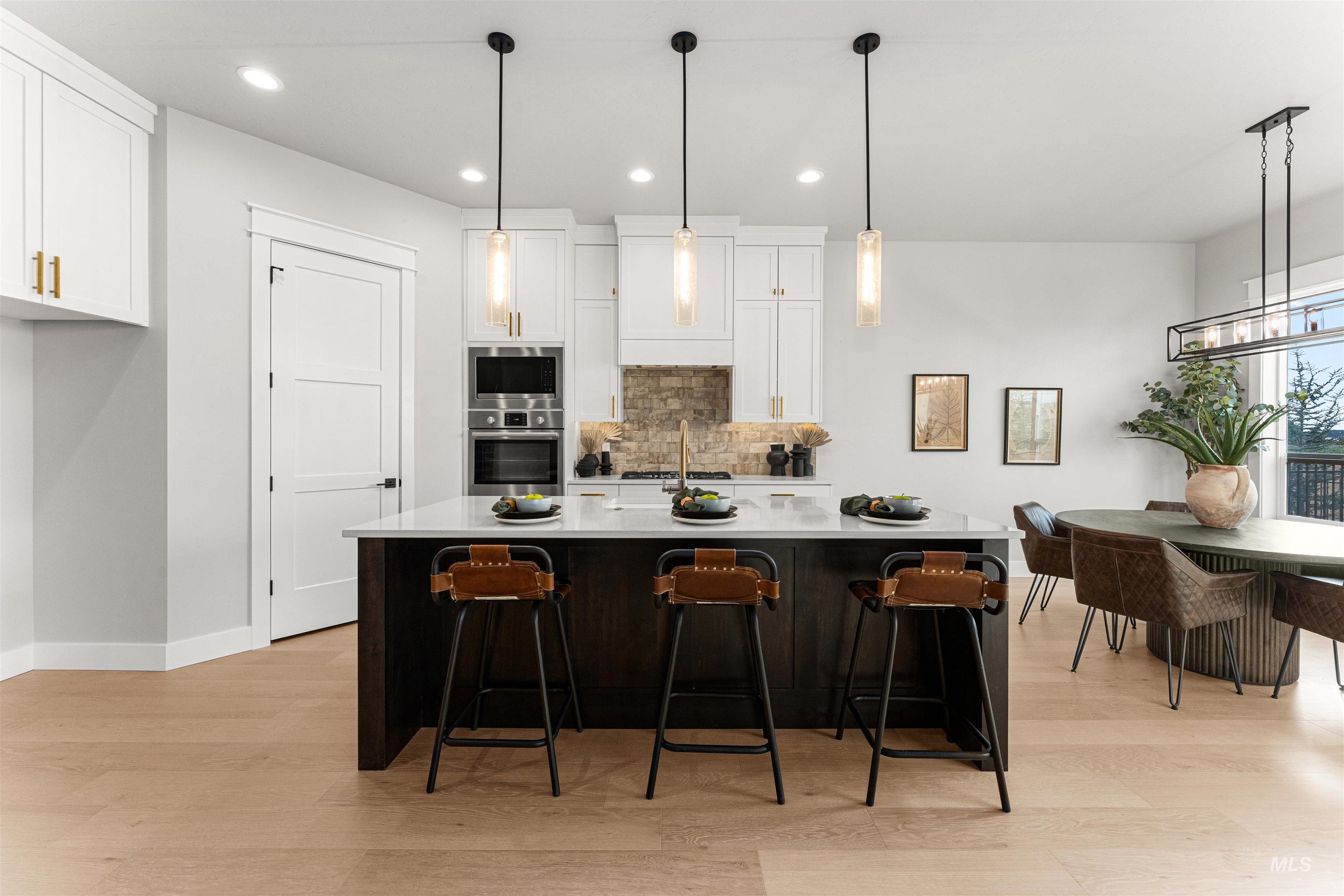 Kitchen featuring white cabinetry, decorative light fixtures, backsplash, recessed lighting, and light wood finished floors
