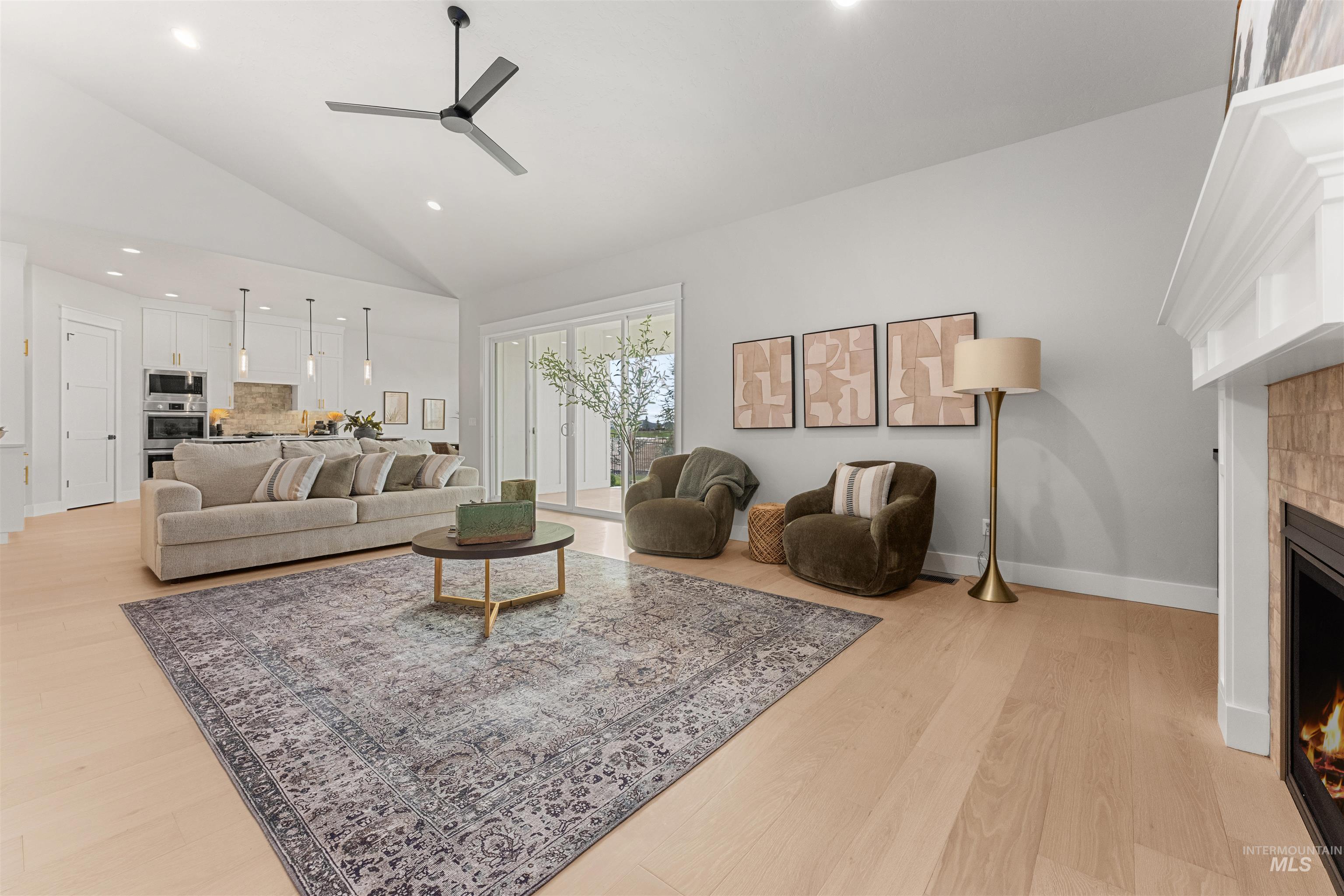 Living room with a warm lit fireplace, recessed lighting, ceiling fan, light wood finished floors, and high vaulted ceiling