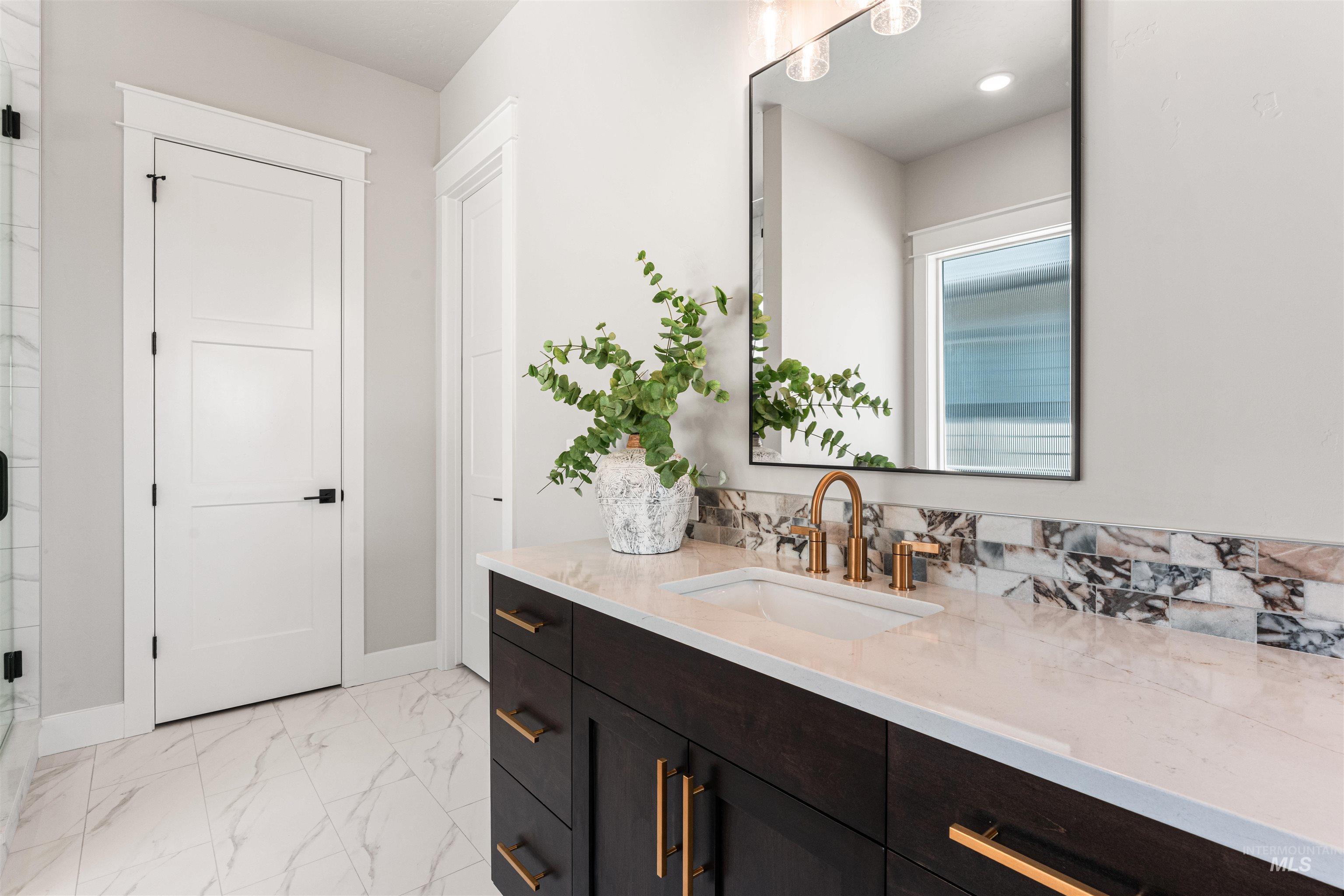 Full bath featuring vanity, marble look tile flooring, and decorative backsplash