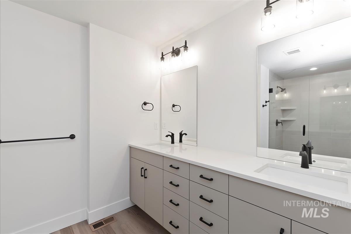 Full bathroom featuring double vanity, light wood finished floors, and tiled shower