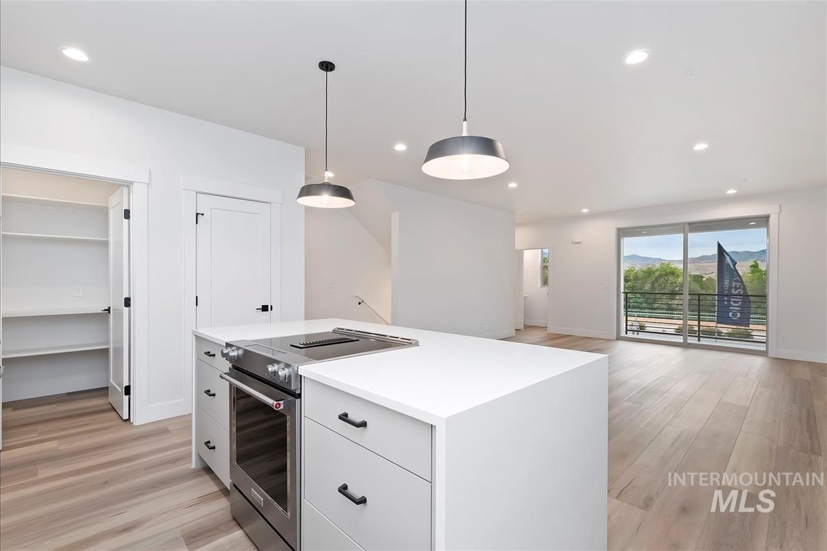 Kitchen with electric stove, white cabinetry, light wood-style floors, decorative light fixtures, and recessed lighting