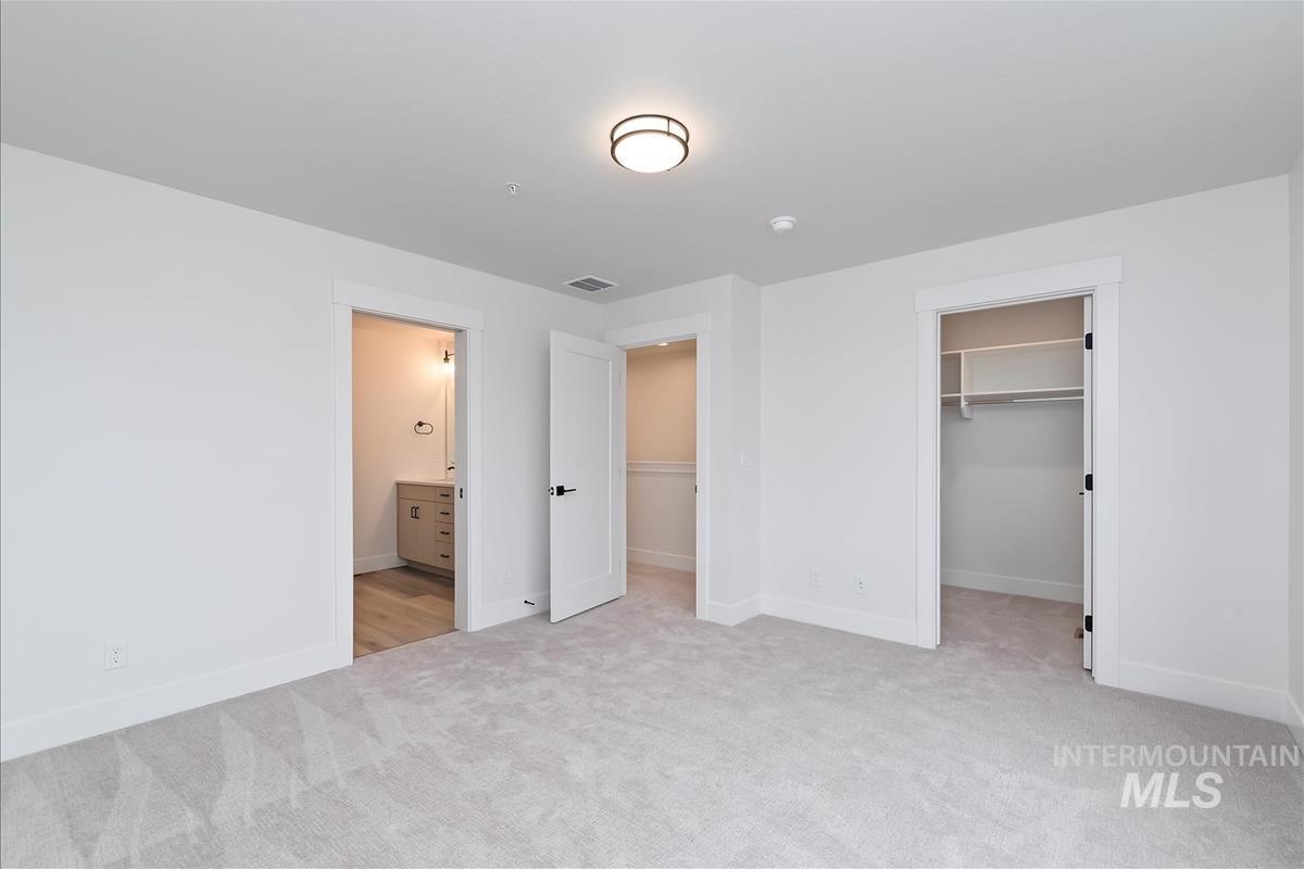 Unfurnished bedroom featuring a spacious closet, light colored carpet, and ensuite bathroom