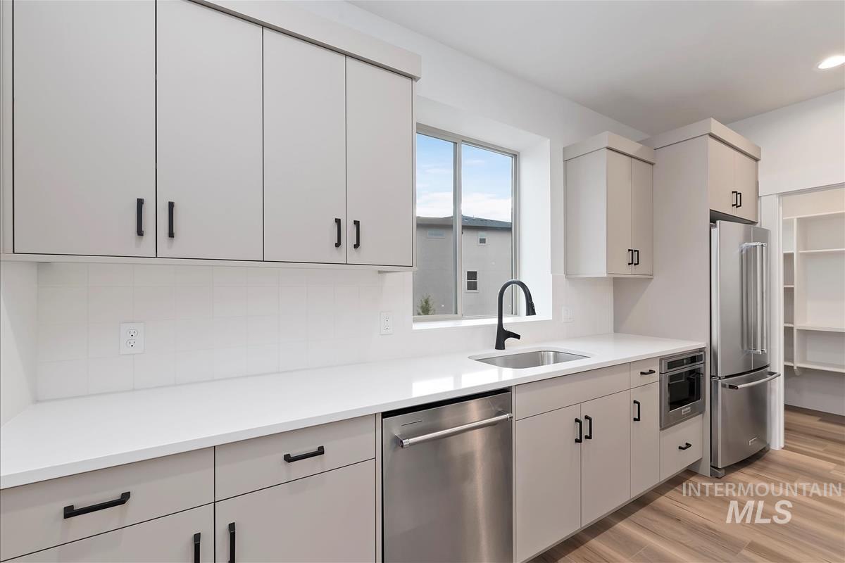 Kitchen with appliances with stainless steel finishes, light wood-style floors, decorative backsplash, and white cabinets