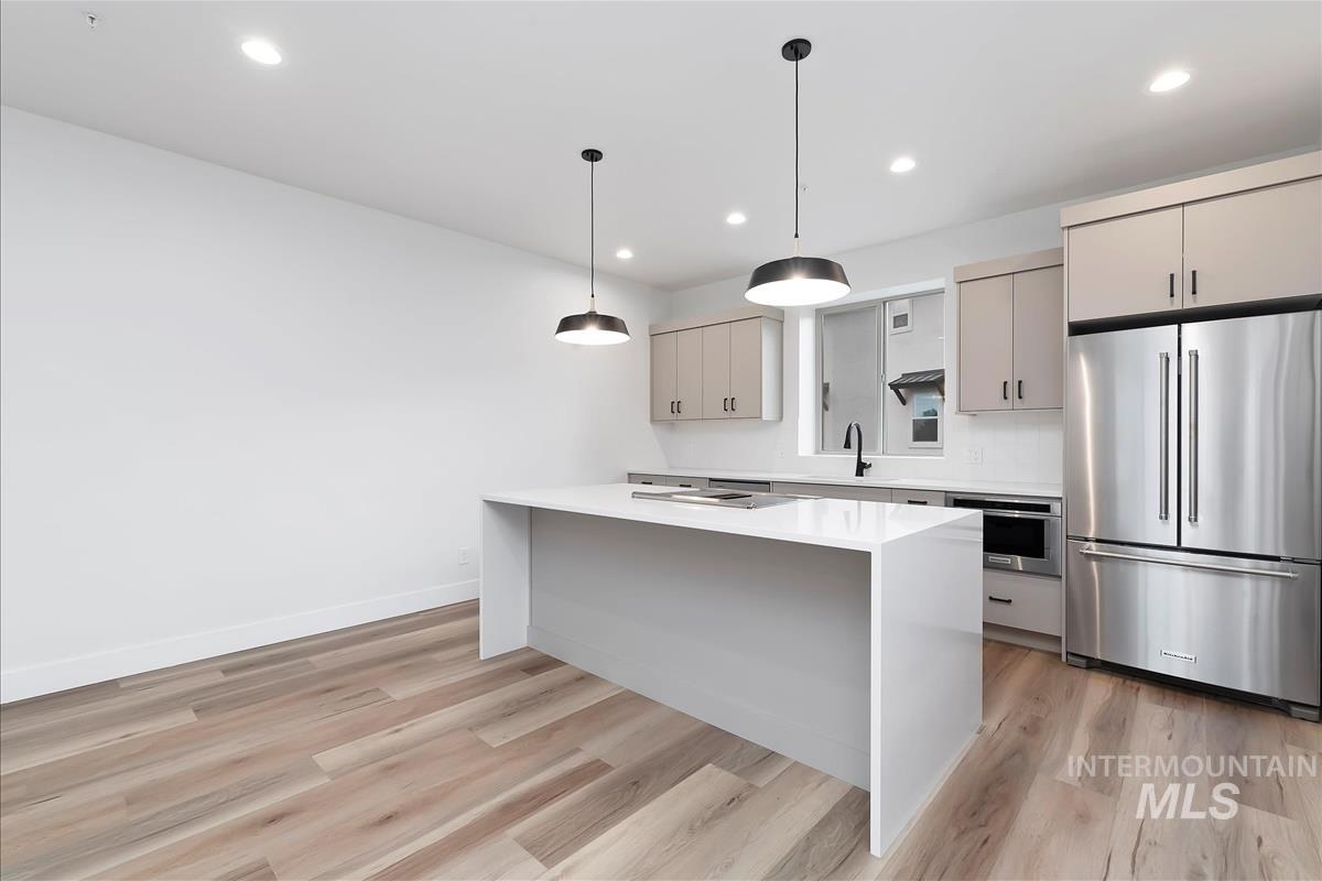 Kitchen featuring appliances with stainless steel finishes, pendant lighting, recessed lighting, light stone counters, and light wood-style flooring