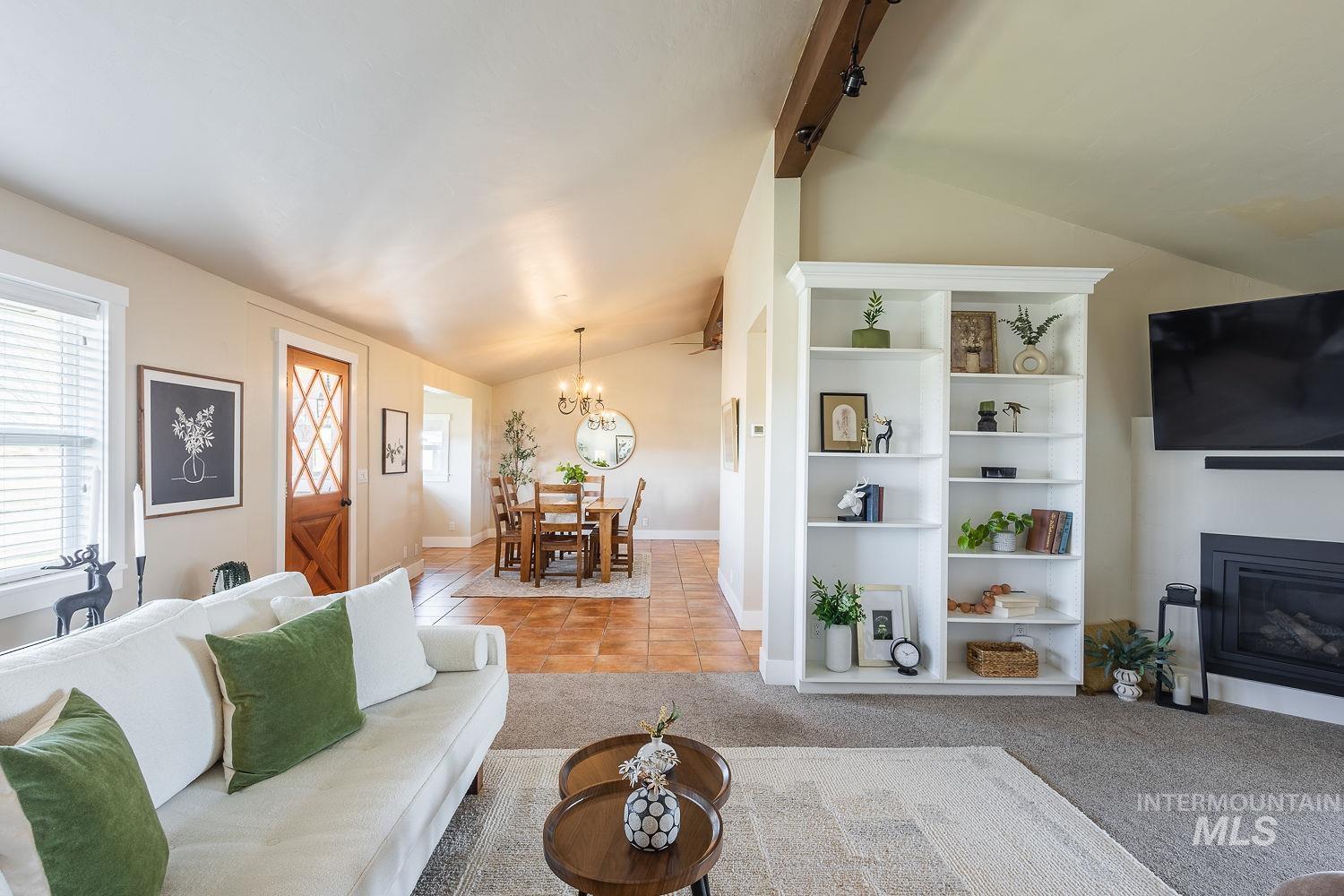 Living area with light tile patterned floors, a glass covered fireplace, a chandelier, and light colored carpet