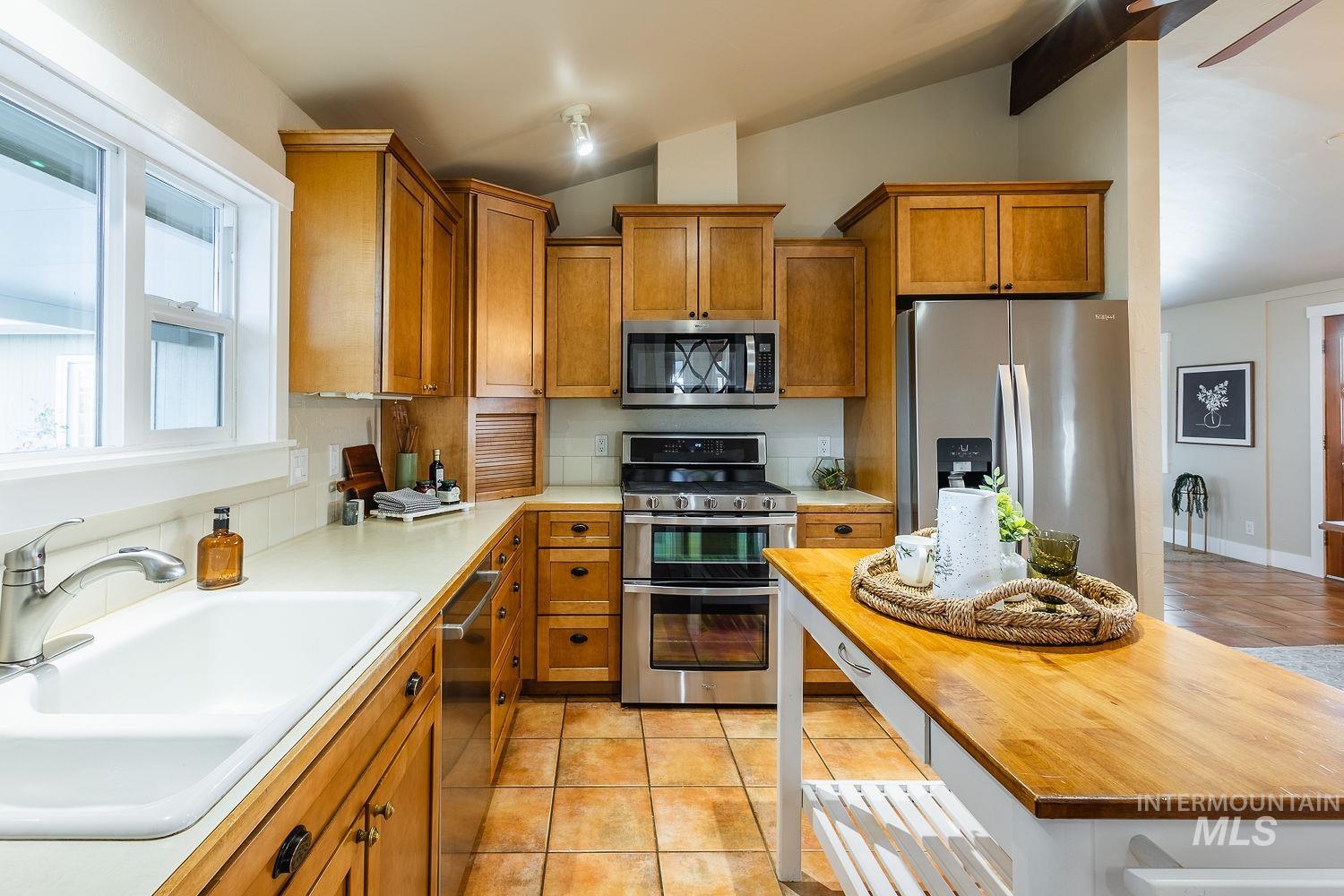 Kitchen with brown cabinetry, appliances with stainless steel finishes, light tile patterned floors, vaulted ceiling, and butcher block counters