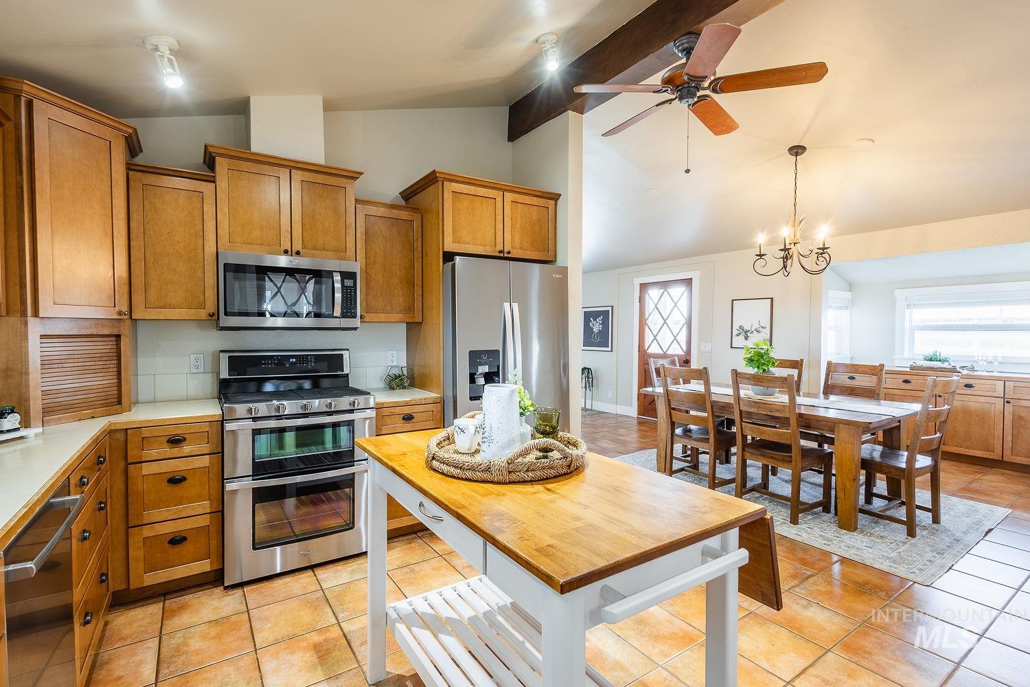 Kitchen with brown cabinets, light countertops, appliances with stainless steel finishes, healthy amount of natural light, and beamed ceiling
