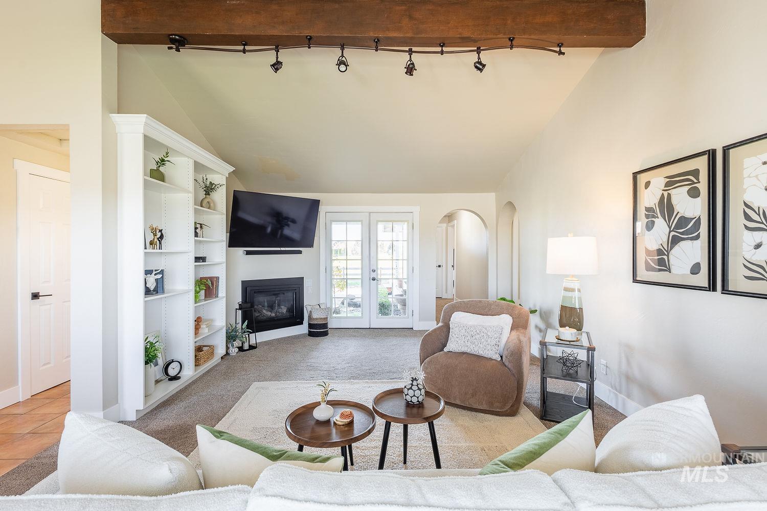 Living area featuring french doors, carpet floors, arched walkways, a glass covered fireplace, and high vaulted ceiling