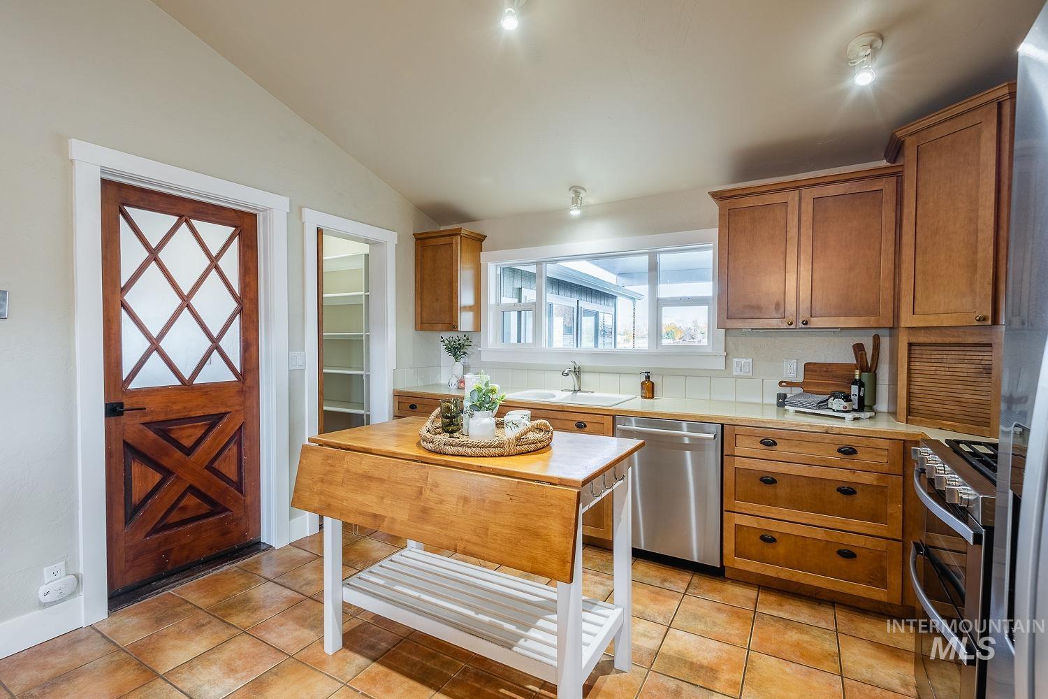 Kitchen featuring light countertops, brown cabinetry, appliances with stainless steel finishes, lofted ceiling, and light tile patterned floors