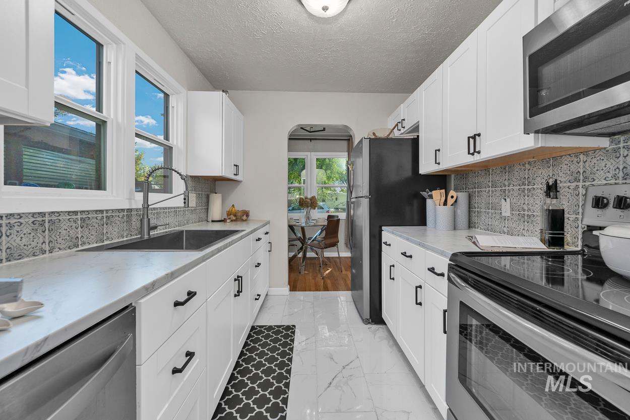Kitchen with appliances with stainless steel finishes, decorative backsplash, light marble finish flooring, arched walkways, and white cabinets
