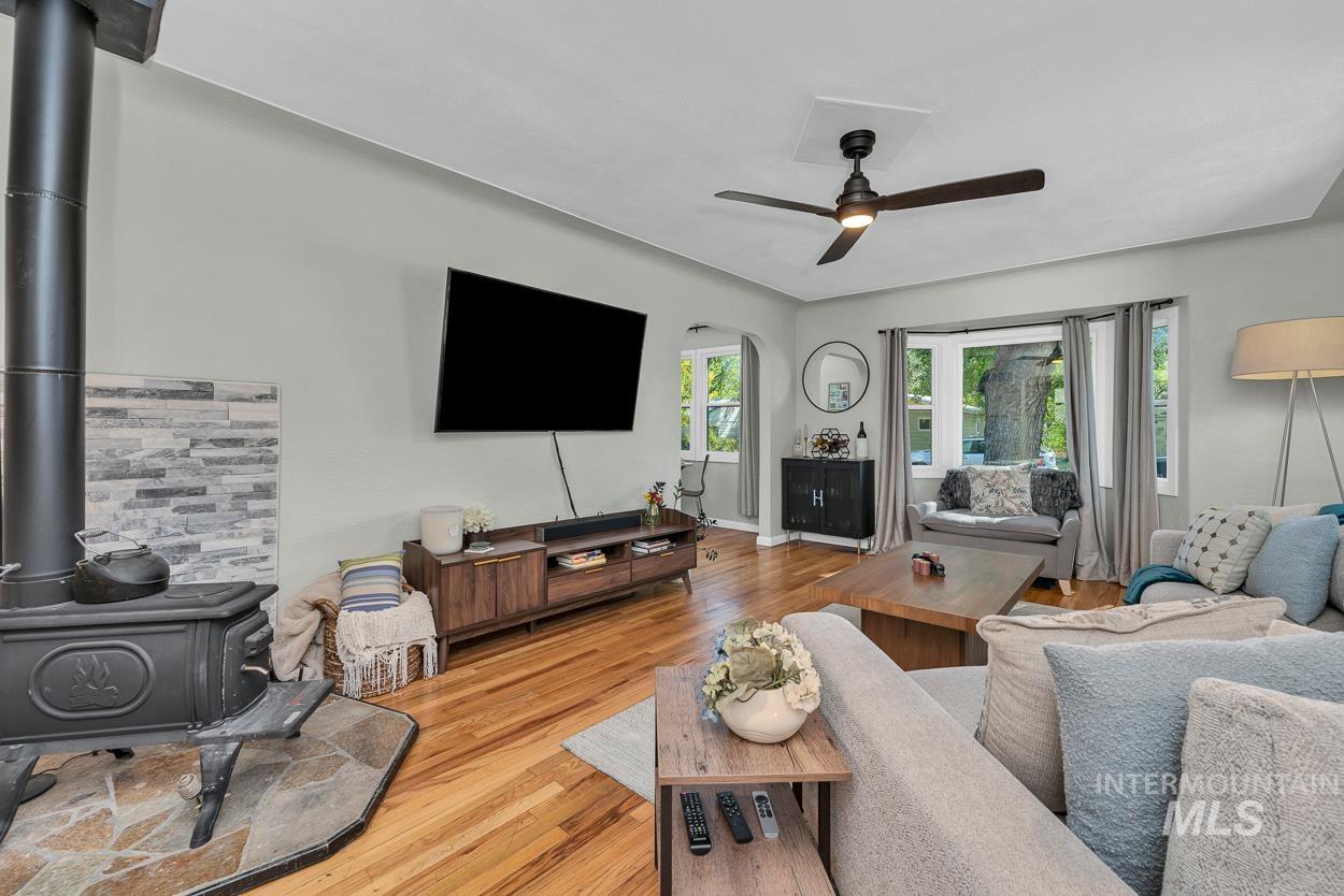 Living area featuring light wood-style flooring, a wood stove, arched walkways, and ceiling fan