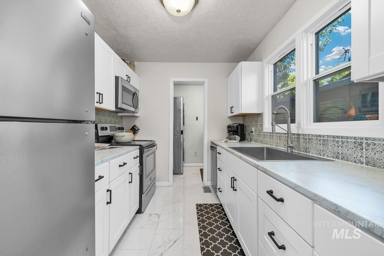 Kitchen featuring stainless steel appliances, white cabinets, light marble finish flooring, backsplash, and a textured ceiling