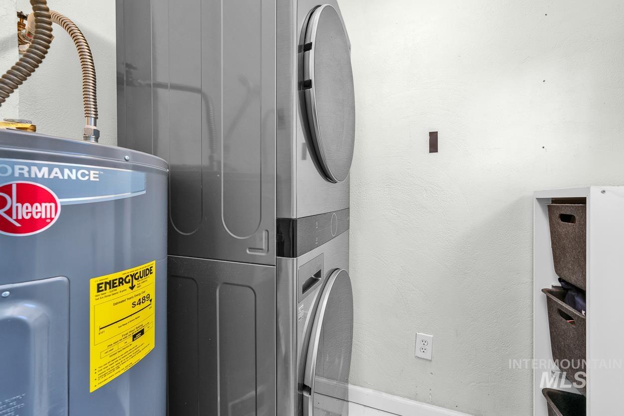 Washroom featuring electric water heater, a textured wall, and stacked washer / drying machine