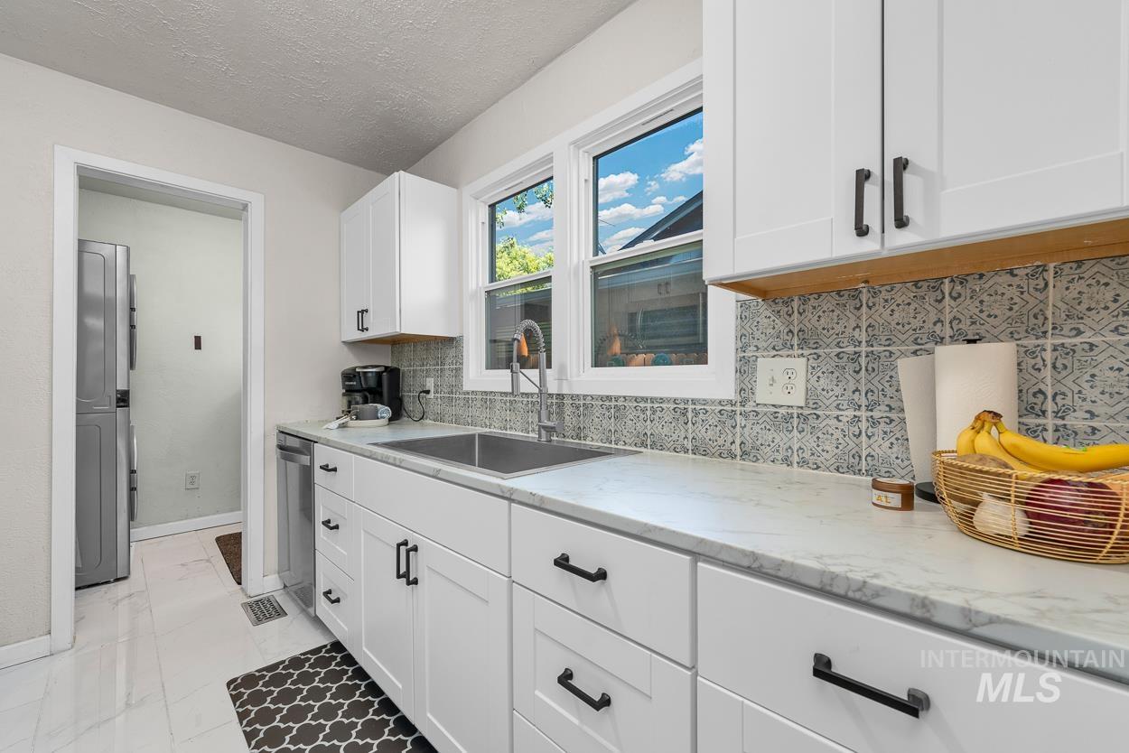 Kitchen featuring decorative backsplash, a textured ceiling, white cabinetry, light stone counters, and washer / clothes dryer