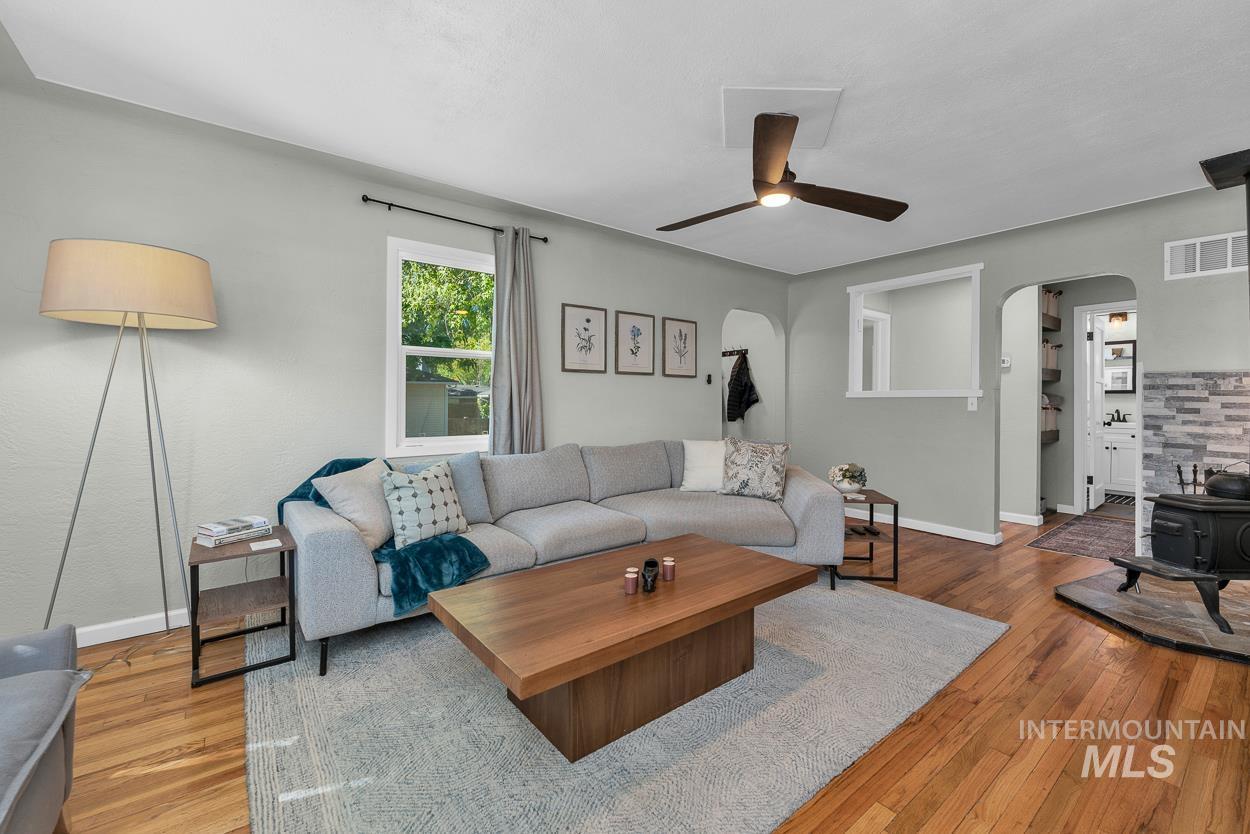 Living room featuring arched walkways, light wood finished floors, a wood stove, and a ceiling fan