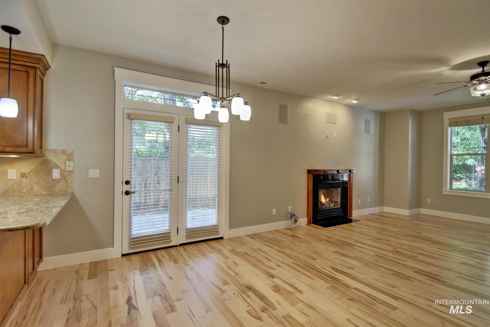 Unfurnished dining area with a fireplace with flush hearth, light wood-style floors, a ceiling fan, and a chandelier