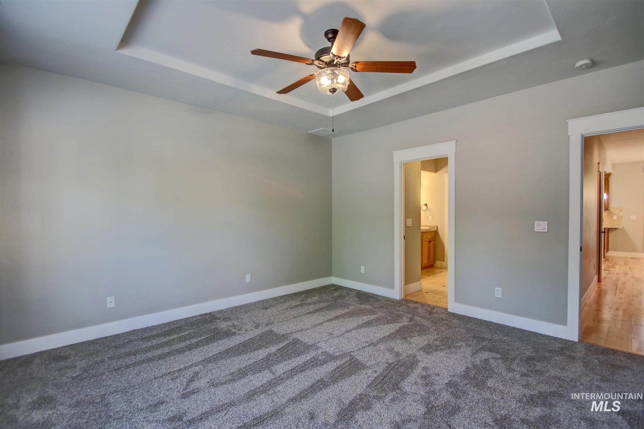Unfurnished bedroom with a raised ceiling, carpet flooring, a ceiling fan, and ensuite bath
