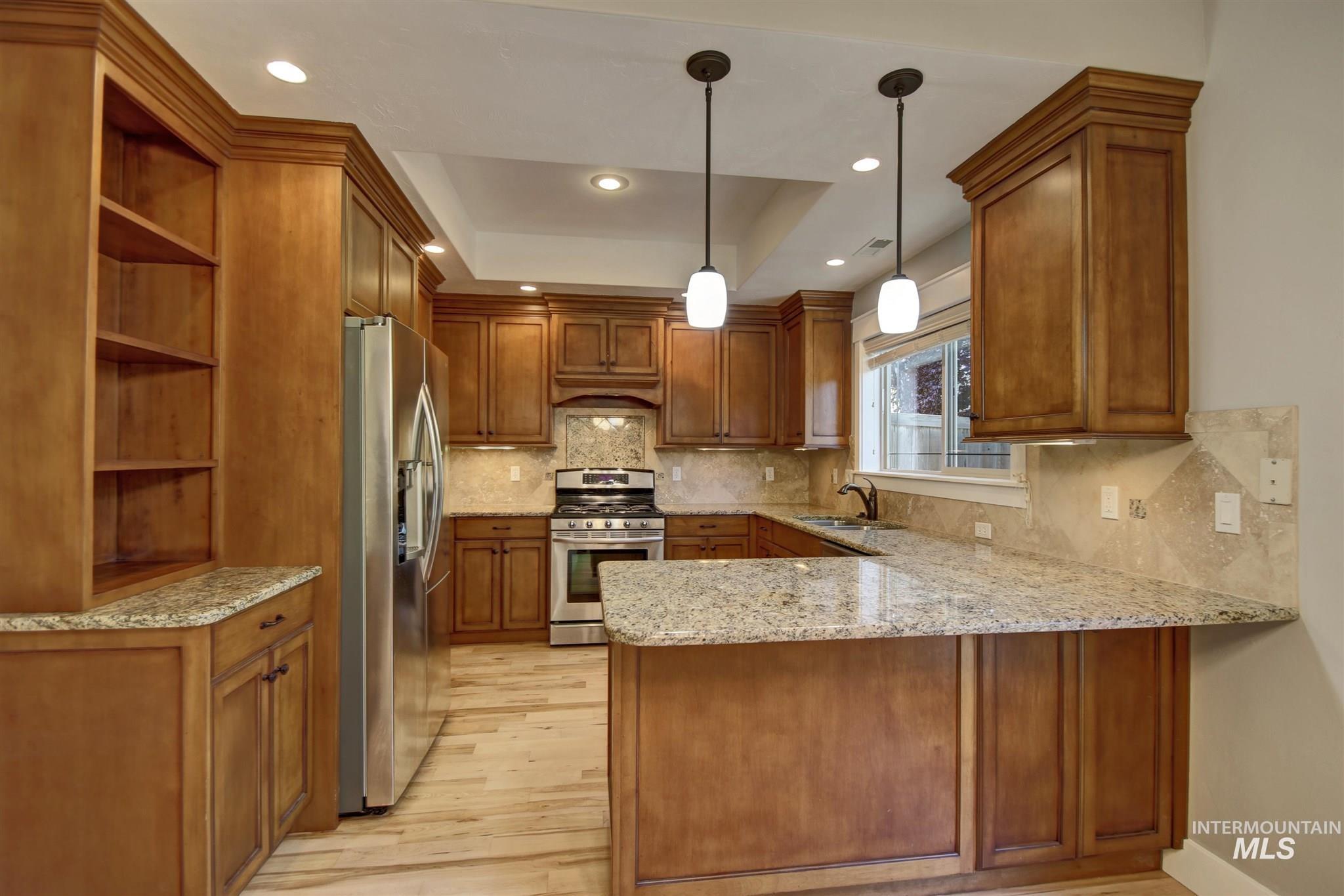 Kitchen featuring brown cabinetry, light stone countertops, a peninsula, stainless steel appliances, and decorative backsplash