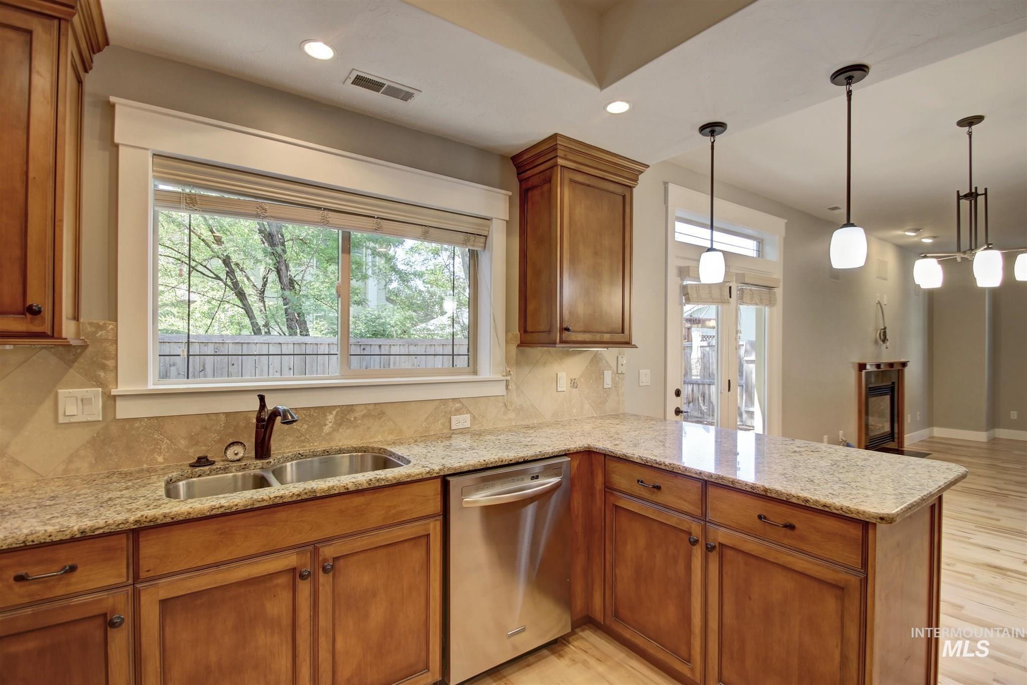Kitchen featuring brown cabinetry, light stone counters, recessed lighting, light wood-style floors, and stainless steel dishwasher