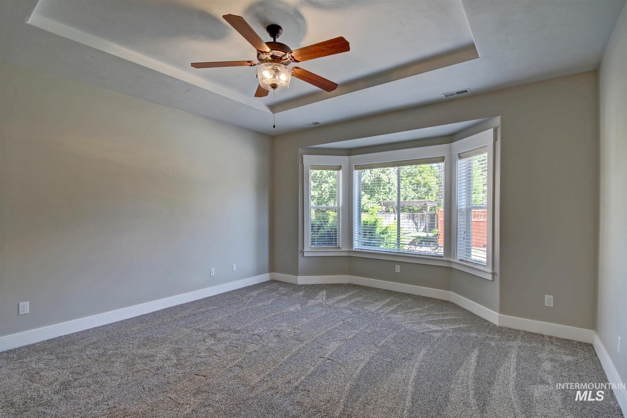 Unfurnished room featuring a raised ceiling, carpet floors, and ceiling fan