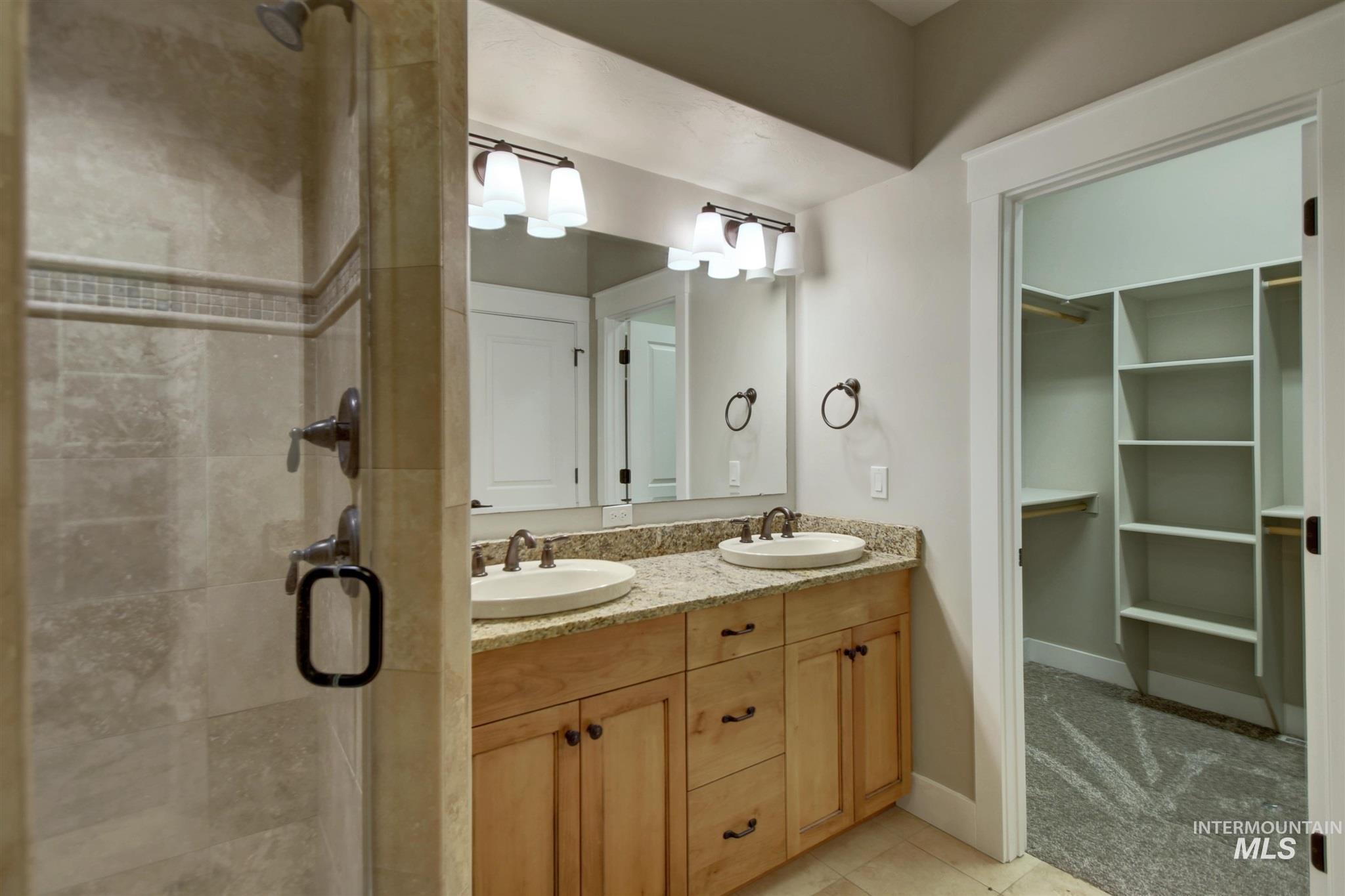 Bathroom with double vanity, light tile patterned floors, and a stall shower