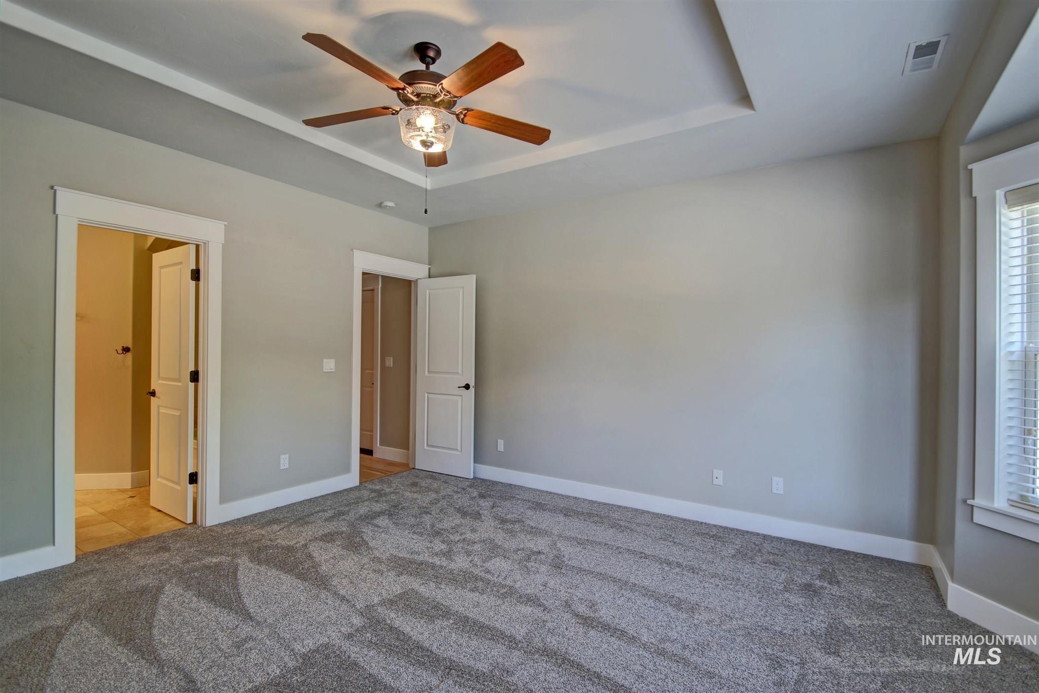 Unfurnished bedroom featuring a tray ceiling, light carpet, ceiling fan, and connected bathroom