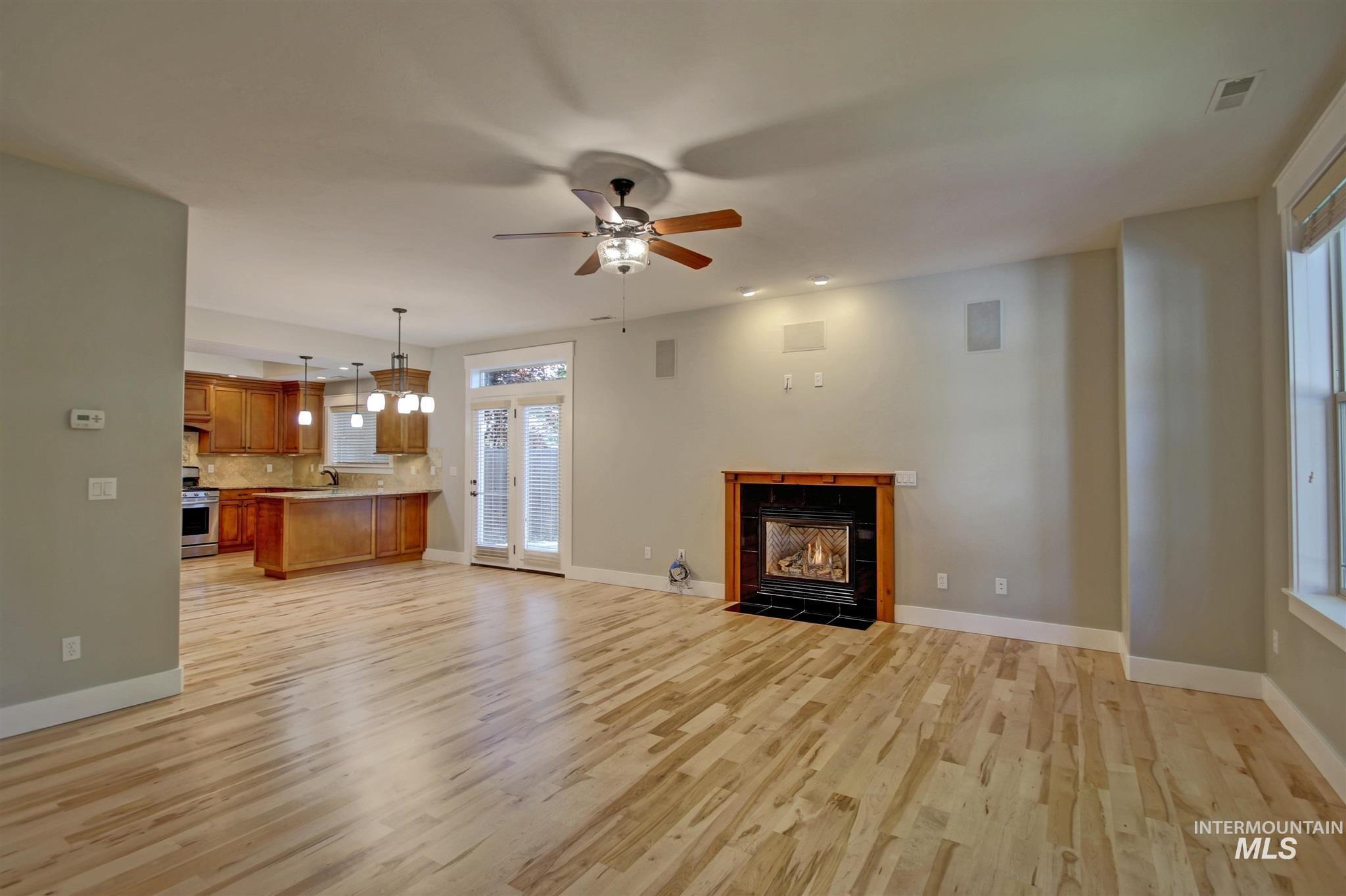 Unfurnished living room featuring a tile fireplace, light wood finished floors, and a ceiling fan