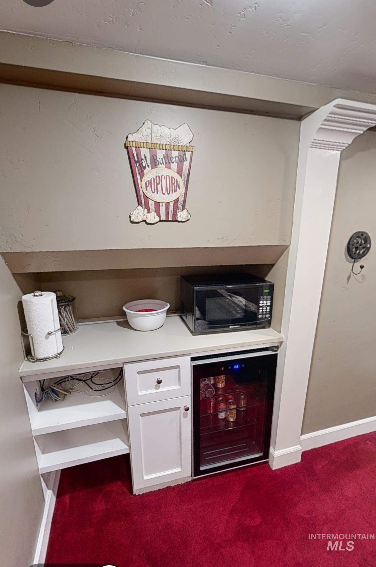 Bar featuring wine cooler, white cabinetry, light countertops, black microwave, and dark carpet
