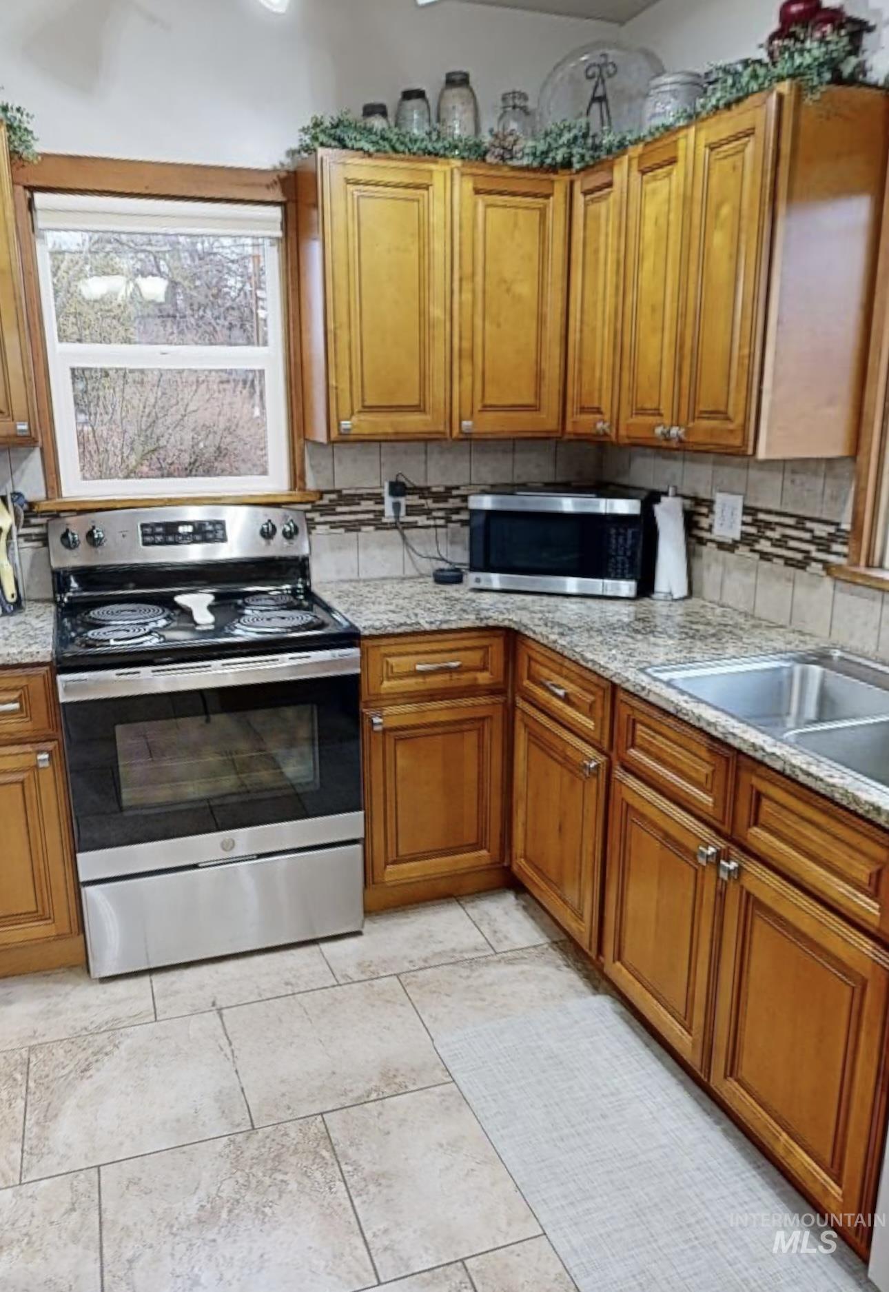 Kitchen featuring tasteful backsplash, stainless steel appliances, wood finish cabinetry, and light stone counters
