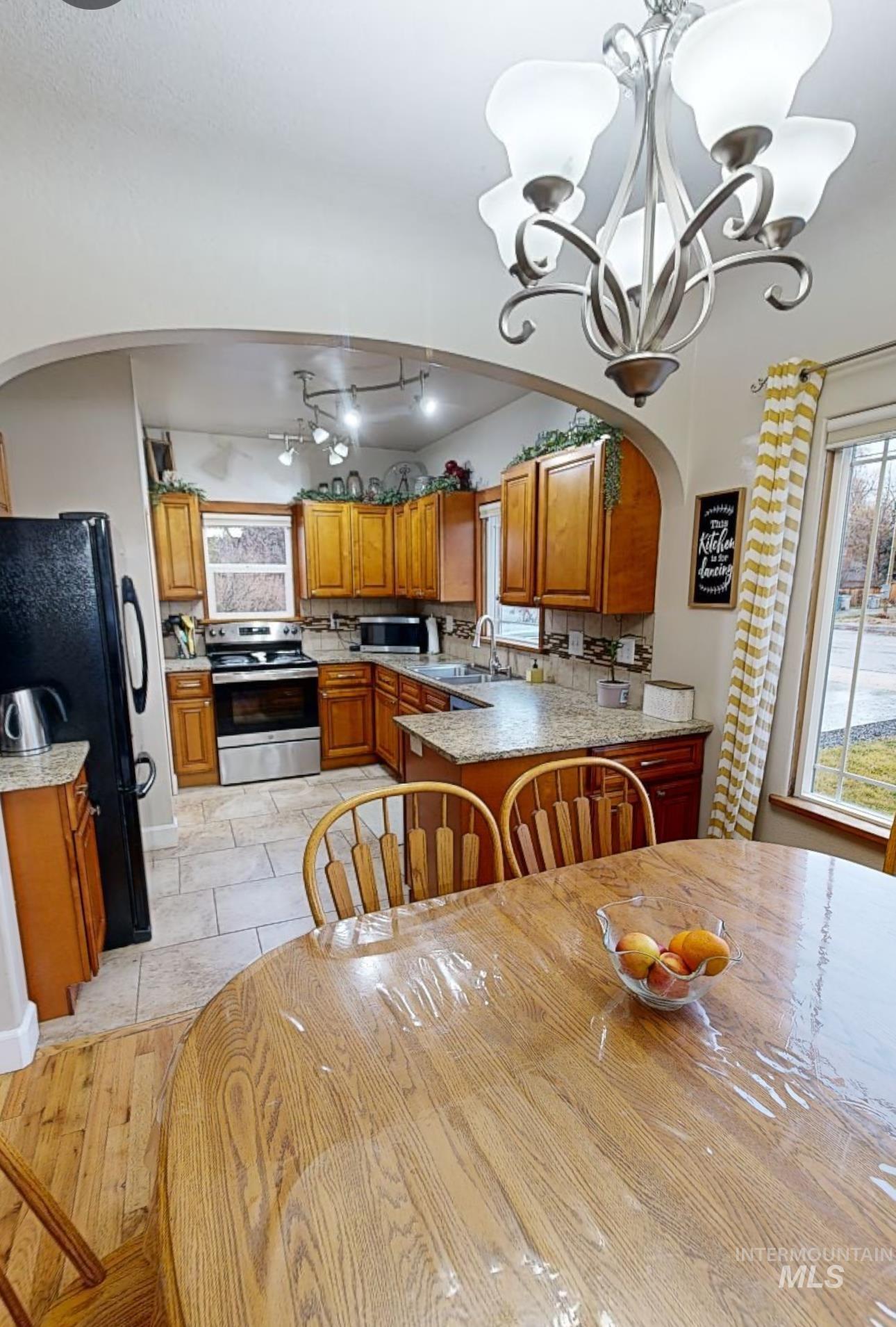 Kitchen featuring arched walkways, stainless steel appliances, light stone counters, and wood finish cabinetry