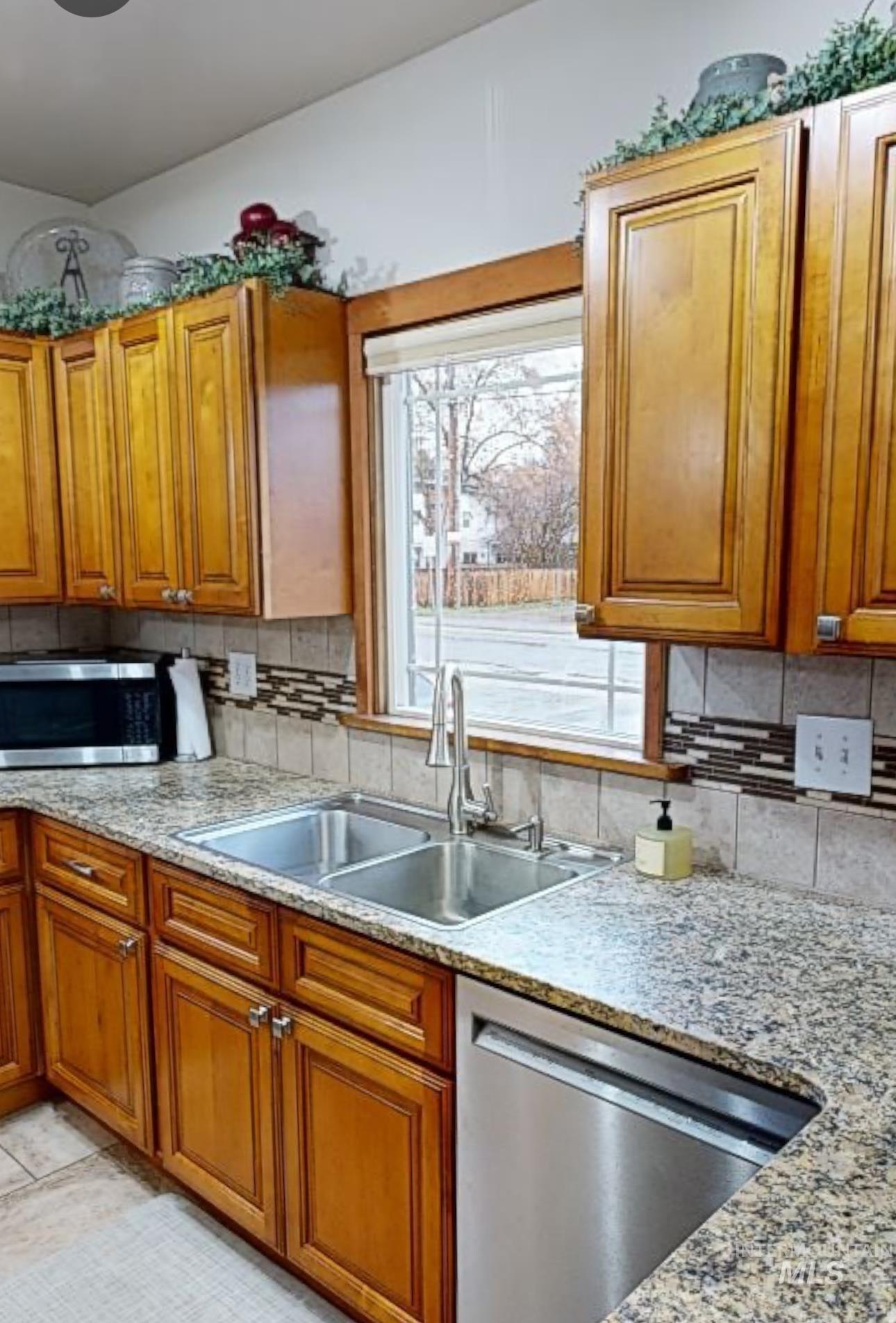 Kitchen with wood finish cabinetry, stainless steel appliances, and light stone counters