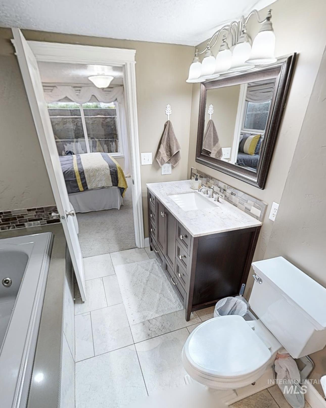 Full bathroom featuring connected bathroom, vanity, a whirlpool tub, backsplash, and light tile patterned flooring