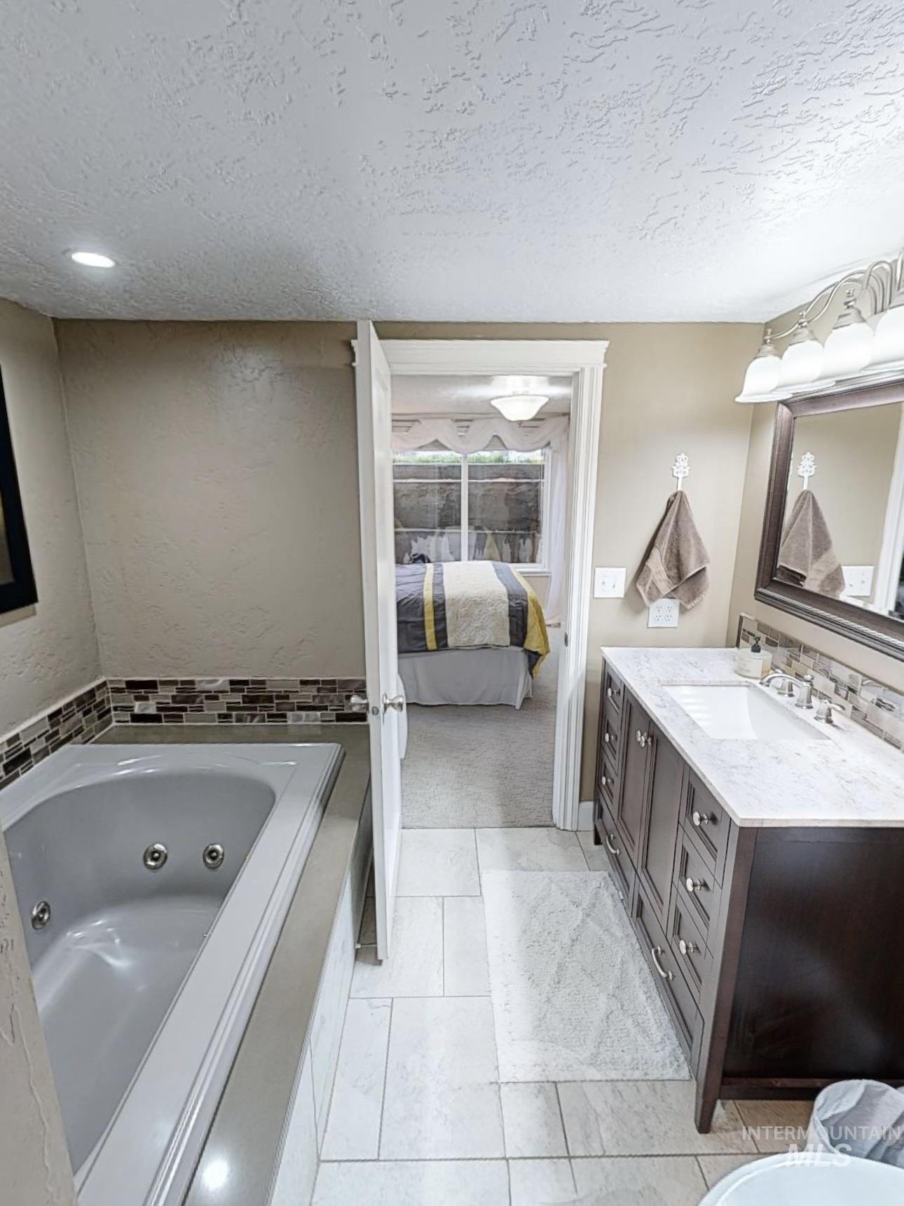 Ensuite bathroom with a textured ceiling, vanity, a jetted tub, and a textured wall