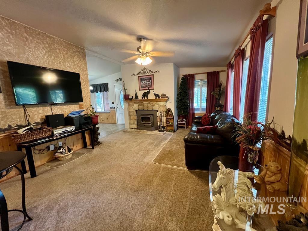 Carpeted living area with a ceiling fan, lofted ceiling, and a stone fireplace