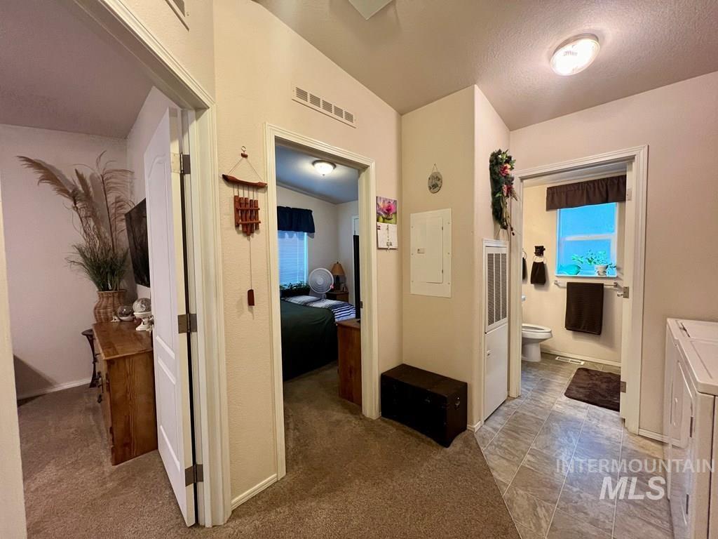 Hallway featuring vaulted ceiling, electric panel, and light colored carpet