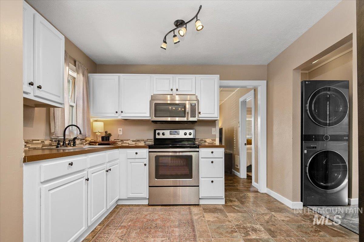 Kitchen with stainless steel appliances, white cabinets, stacked washing machine and dryer, stone finish flooring, and dark countertops