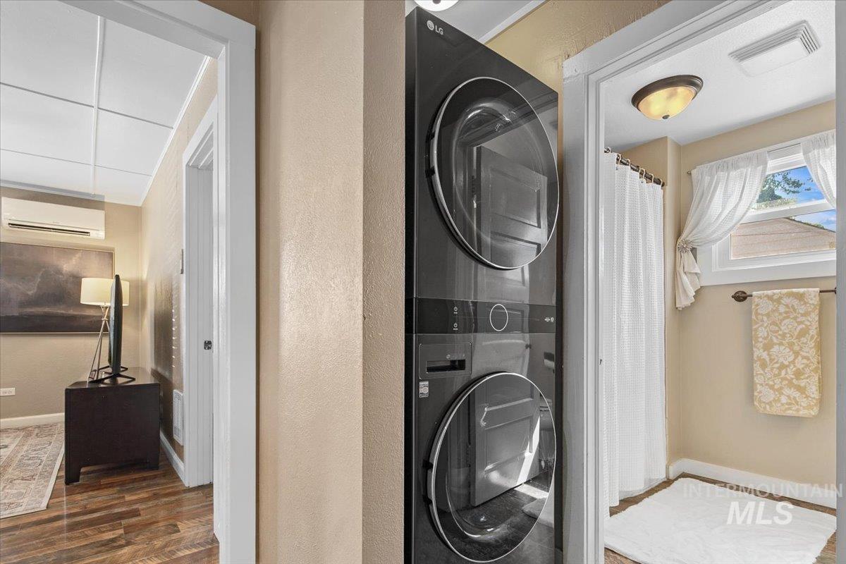 Washroom with dark wood finished floors, stacked washer / drying machine, a wall unit AC, and a textured wall