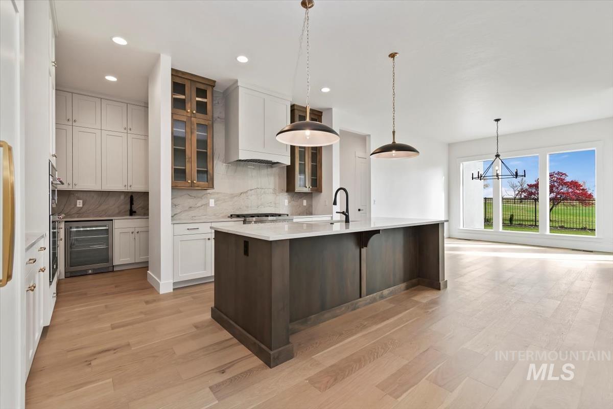 Kitchen featuring glass insert cabinets, a kitchen breakfast bar, beverage cooler, a center island with sink, and tasteful backsplash