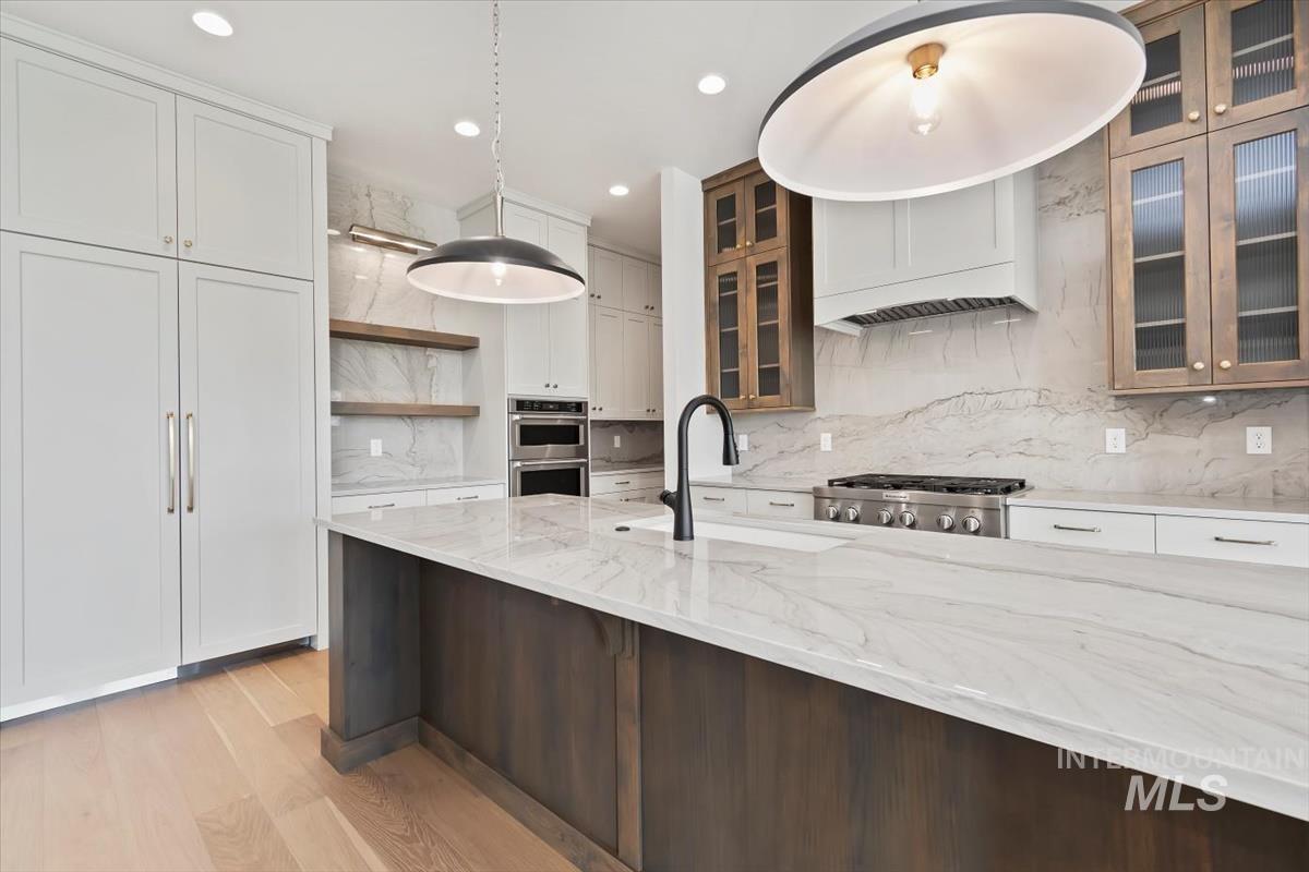 Kitchen featuring glass insert cabinets, backsplash, light stone counters, and recessed lighting