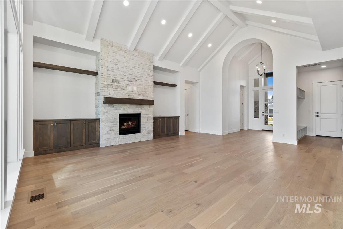 Unfurnished living room featuring high vaulted ceiling, light wood finished floors, a stone fireplace, arched walkways, and beam ceiling