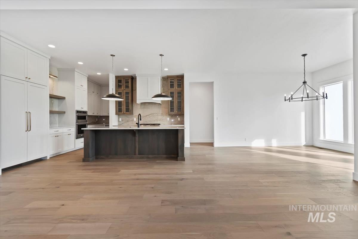 Kitchen featuring glass insert cabinets, open floor plan, open shelves, tasteful backsplash, and a kitchen island with sink